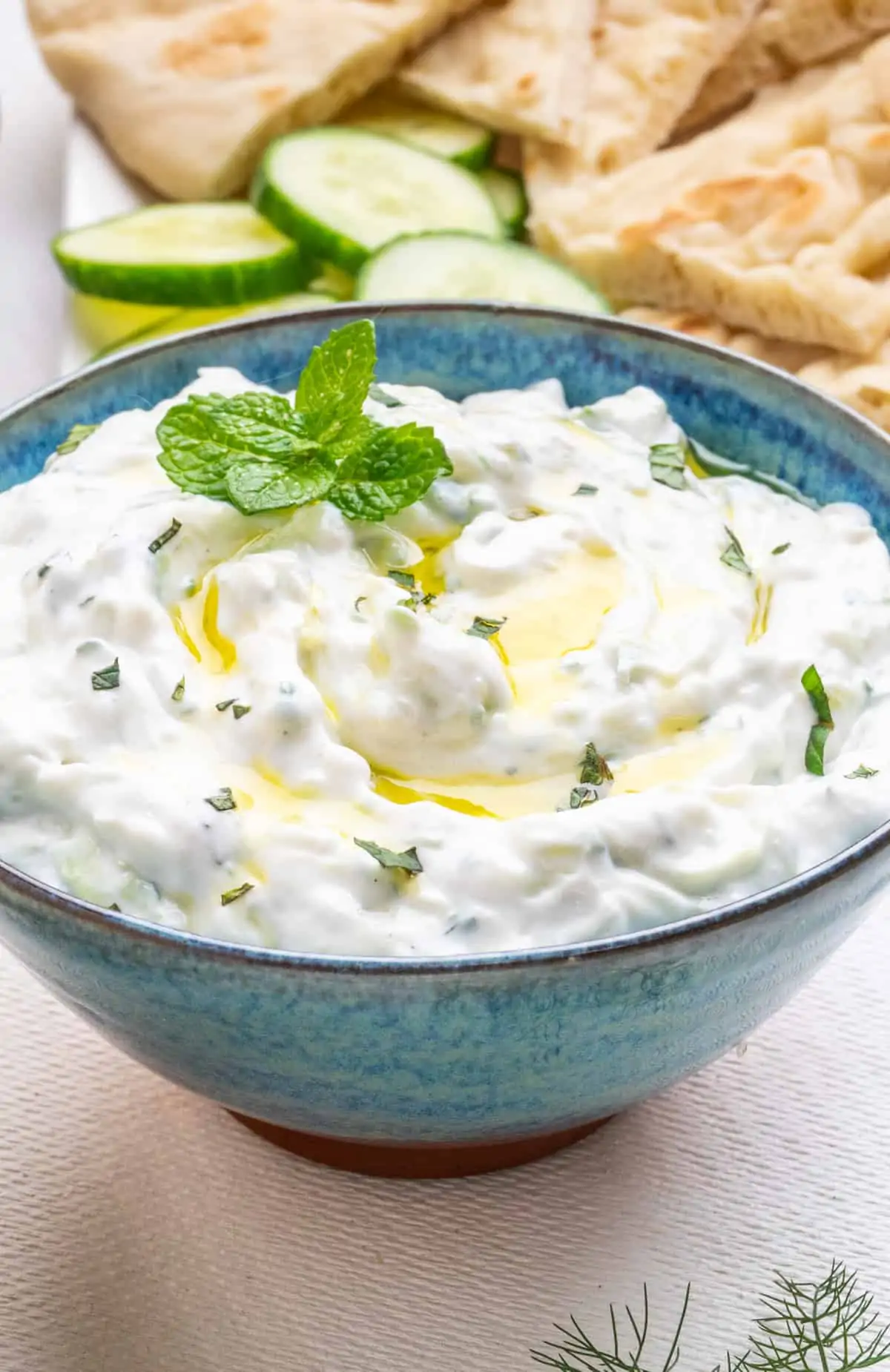 tzatziki sauce topped with olive oil and herbs in a blue bowl.