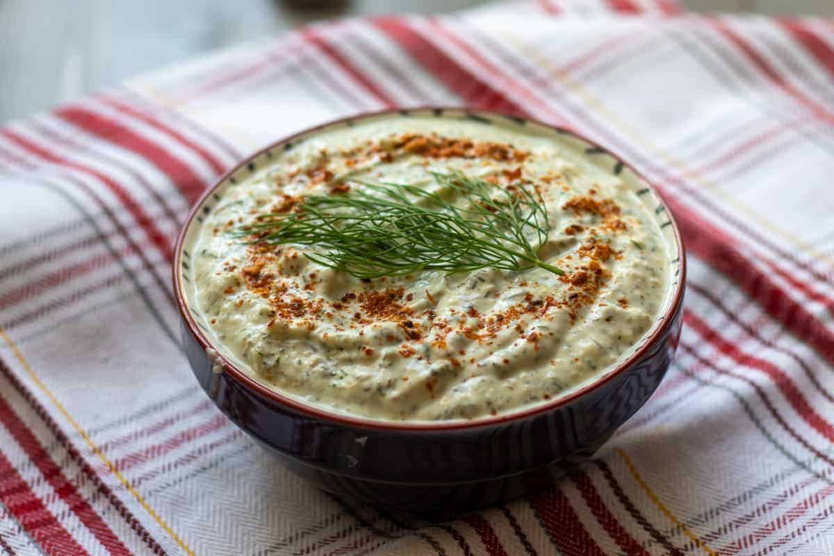 creamy green sauce in a dark red ceramic bowl on a plaid tablecloth.