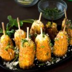 grilled mexican corn on the cob on sticks on a black plate.