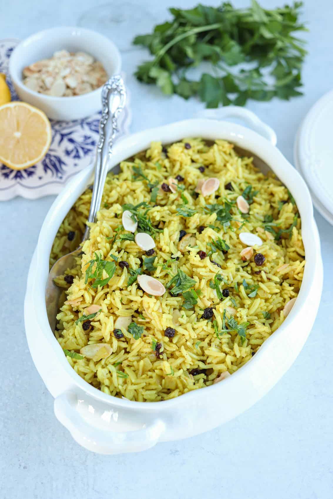 yellow rice with sliced almonds, currants and fresh parsley in a white oval serving dish.