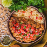 pinto beans and rice in a round brown bowl topped with pico de gallo.