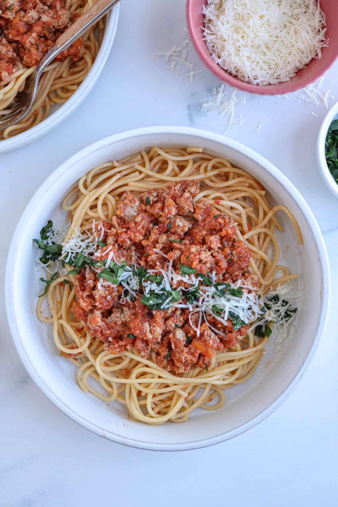 spaghetti with pork bolognese sauce sprinkled with parmesan cheese and chopped parsley in a gray bowl.