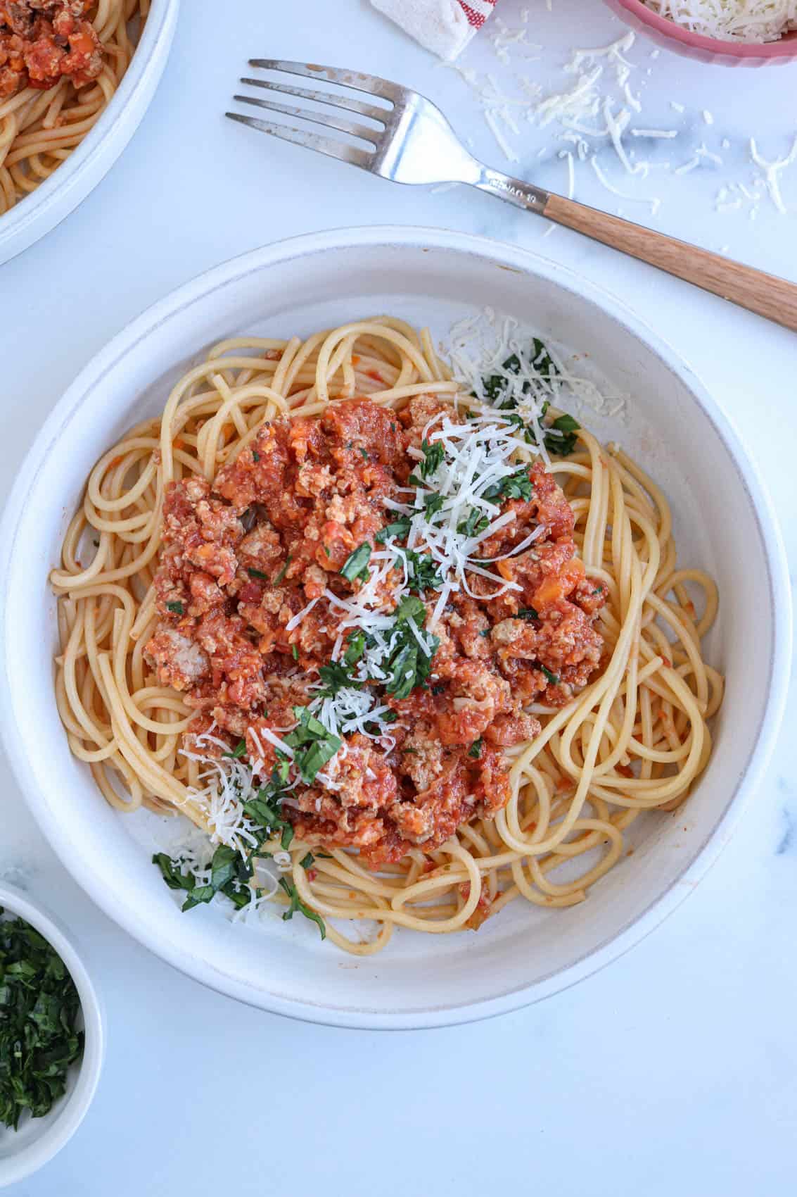 spaghetti with pork bolognese sauce sprinkled with parmesan cheese and chopped parsley in a gray bowl.