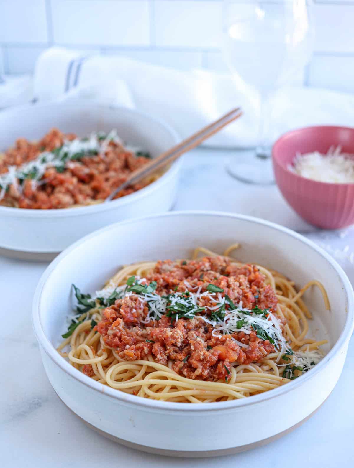spaghetti with pork bolognese sauce sprinkled with parmesan cheese and chopped parsley in a gray bowl.