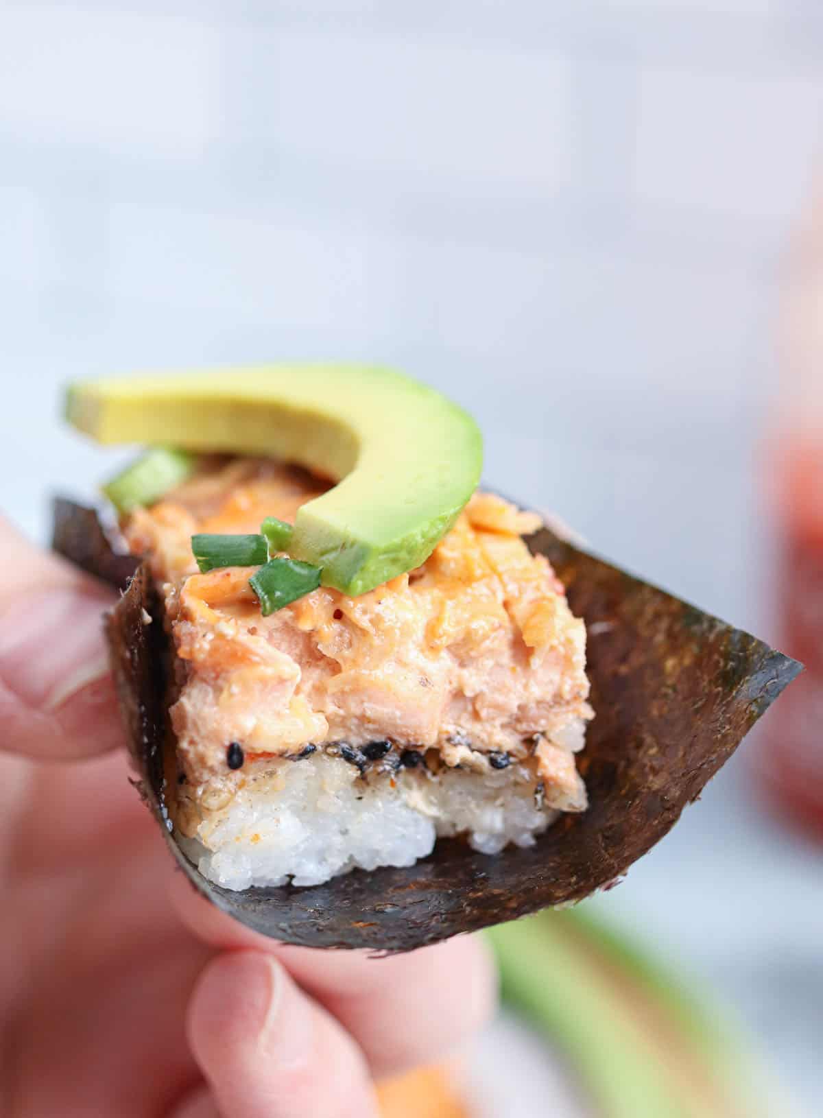 one salmon sushi bake piece served on a small nori sheet with a slice of avocado and scallions on top.