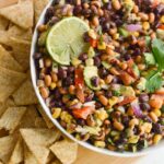 bean salad in a white bowl surrounded by corn chips.