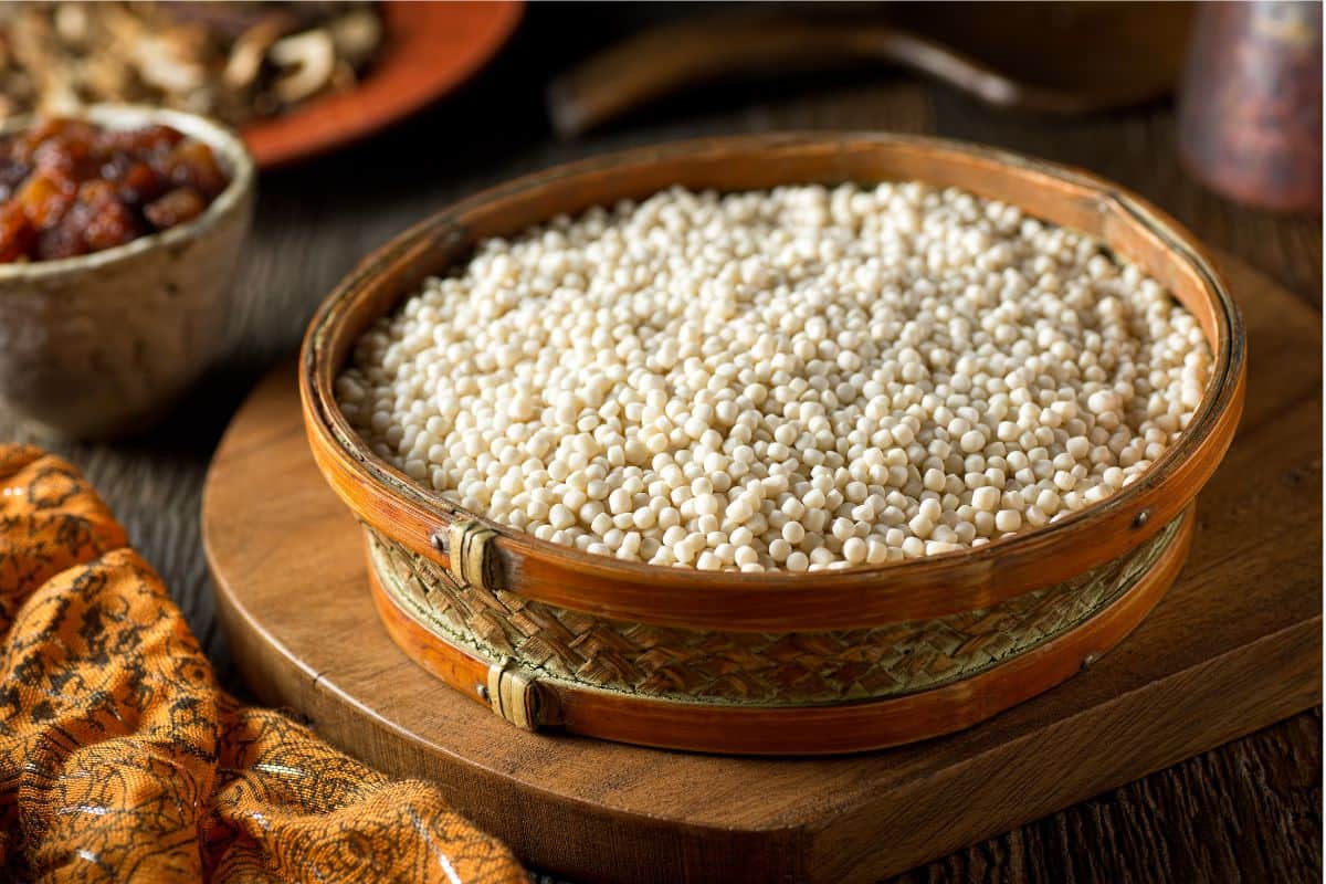 uncooked Israeli couscous in a wooden bowl on a wooden board.