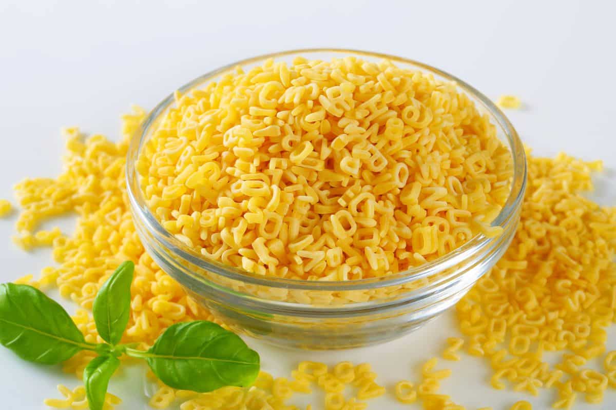 uncooked alphabet pasta in a glass bowl.
