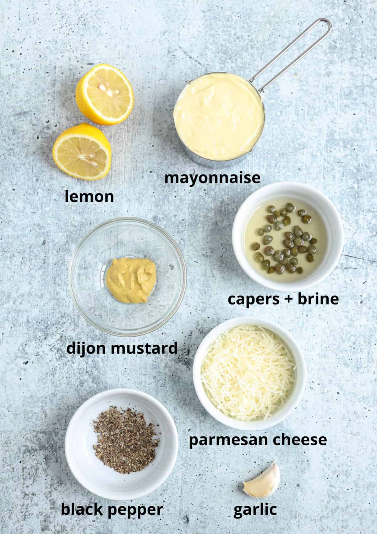 ingredients for making caesar salad dressing on a gray surface with captions.