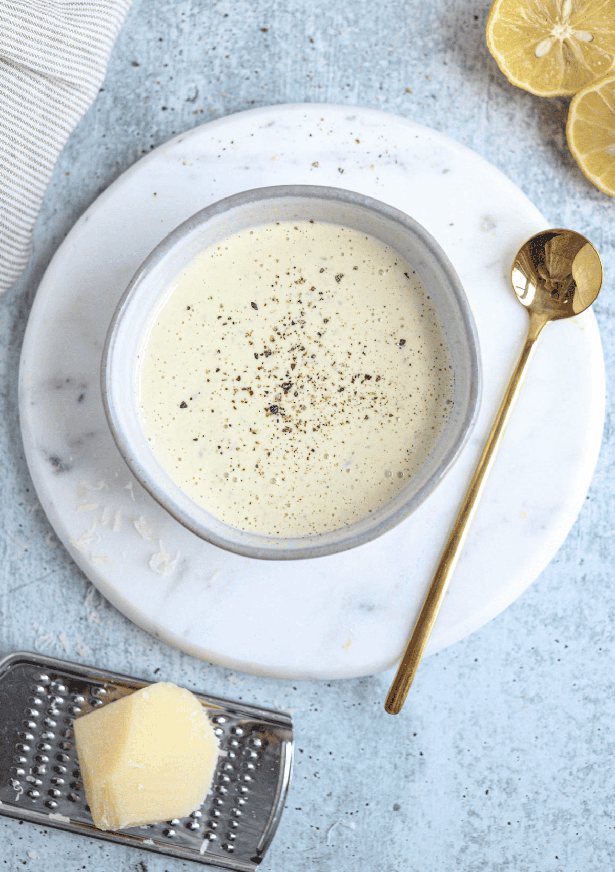 caesar salad dressing in a small gray bowl on a white marble board.