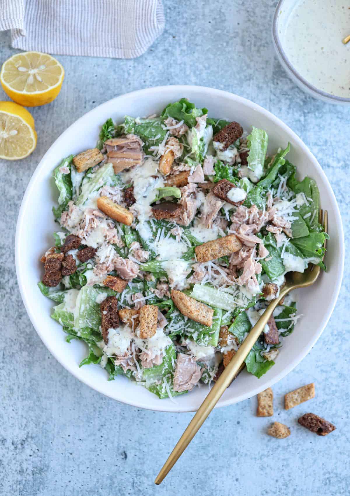 caesar salad wth coutons , tuna, parmesan cheese and dressing in a white bowl.
