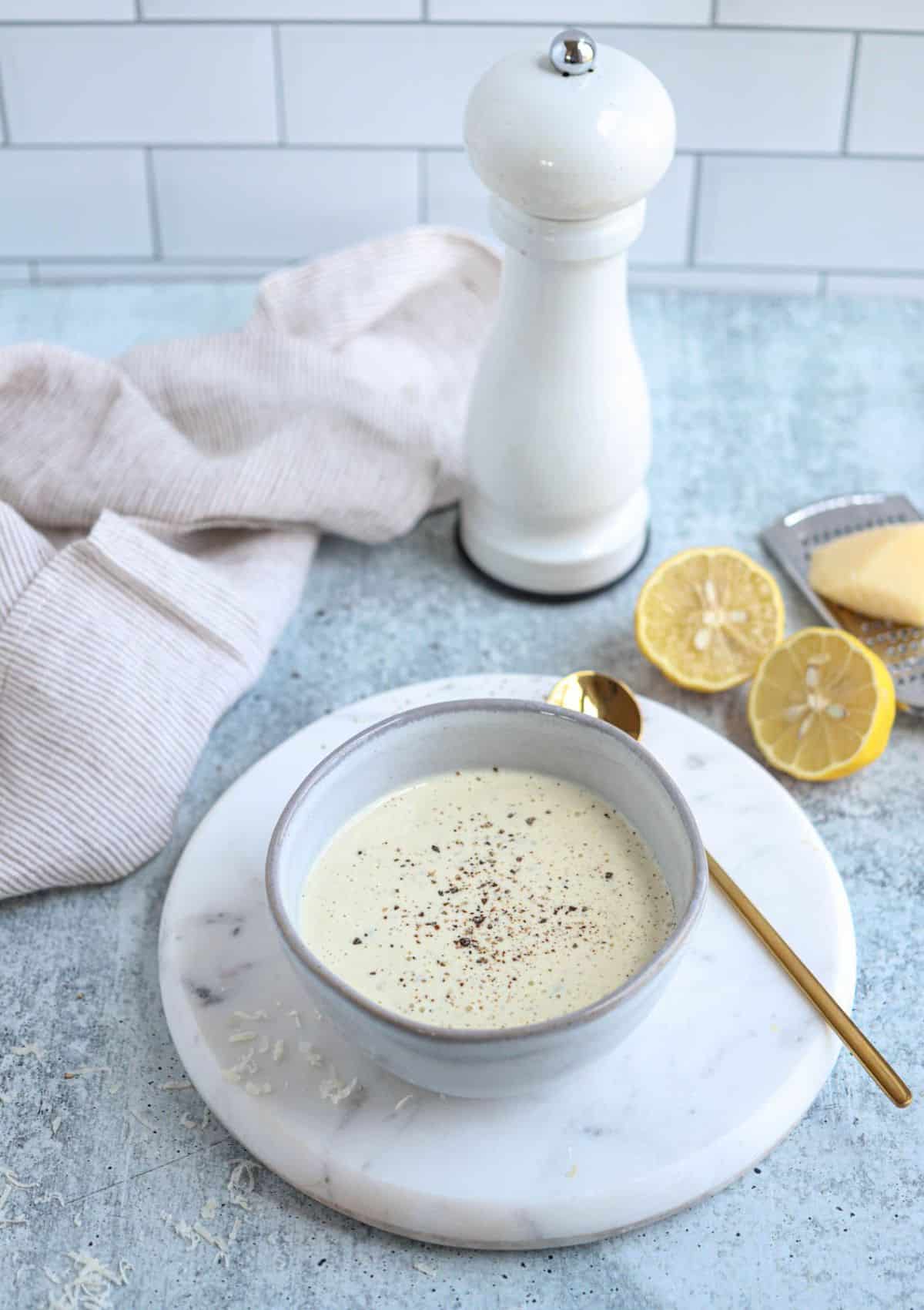 caesar salad dressing in a small gray bowl on a white marble board.