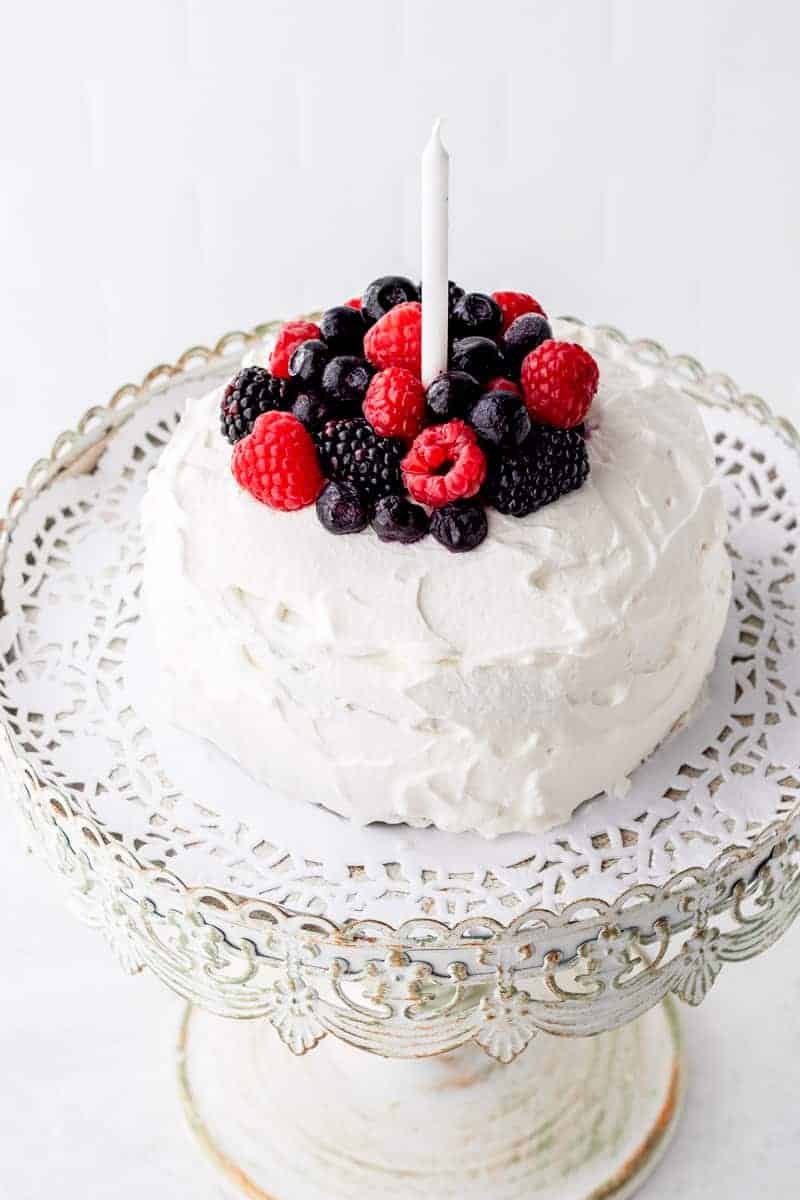 a small cake iced with vanilla frosting topped with fresh berries and a single candle. 