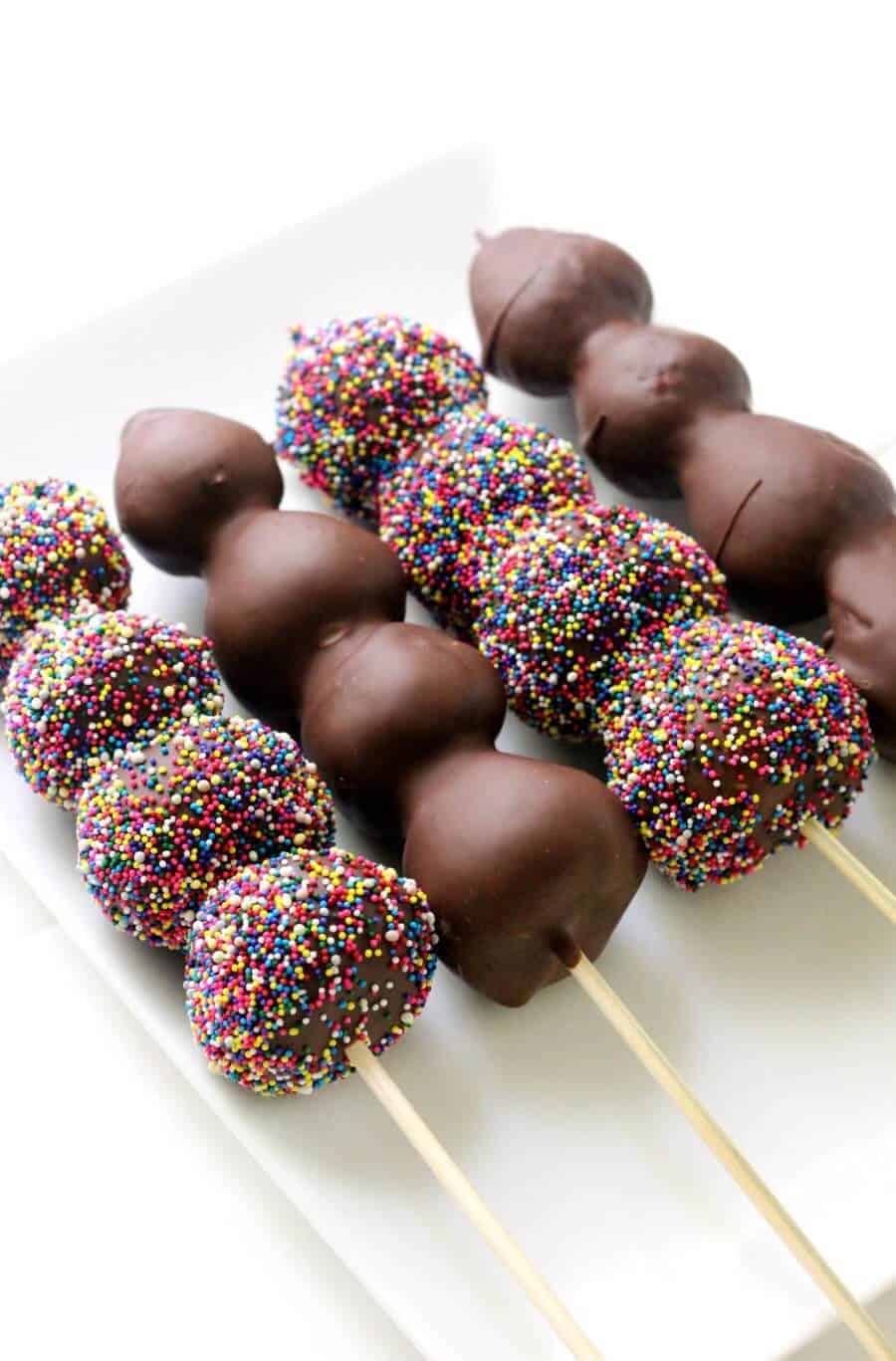 chocolate covered strawberries on sticks with rainbow sprinkles on a plate.