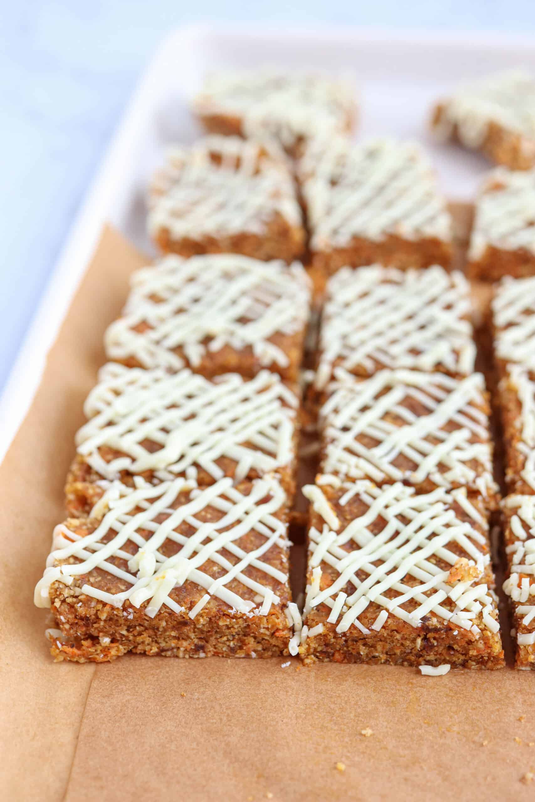 raw carrot cake bars drizzled with white chocolate on a cookie sheet.