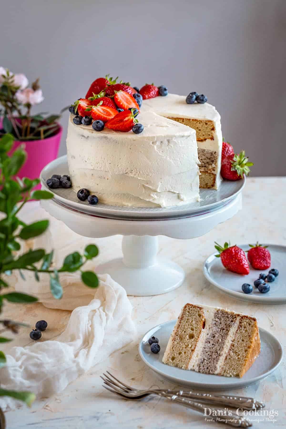 yellow cashew cake frosted with vanilla icing and topped with fresh berries on a cake stand. 