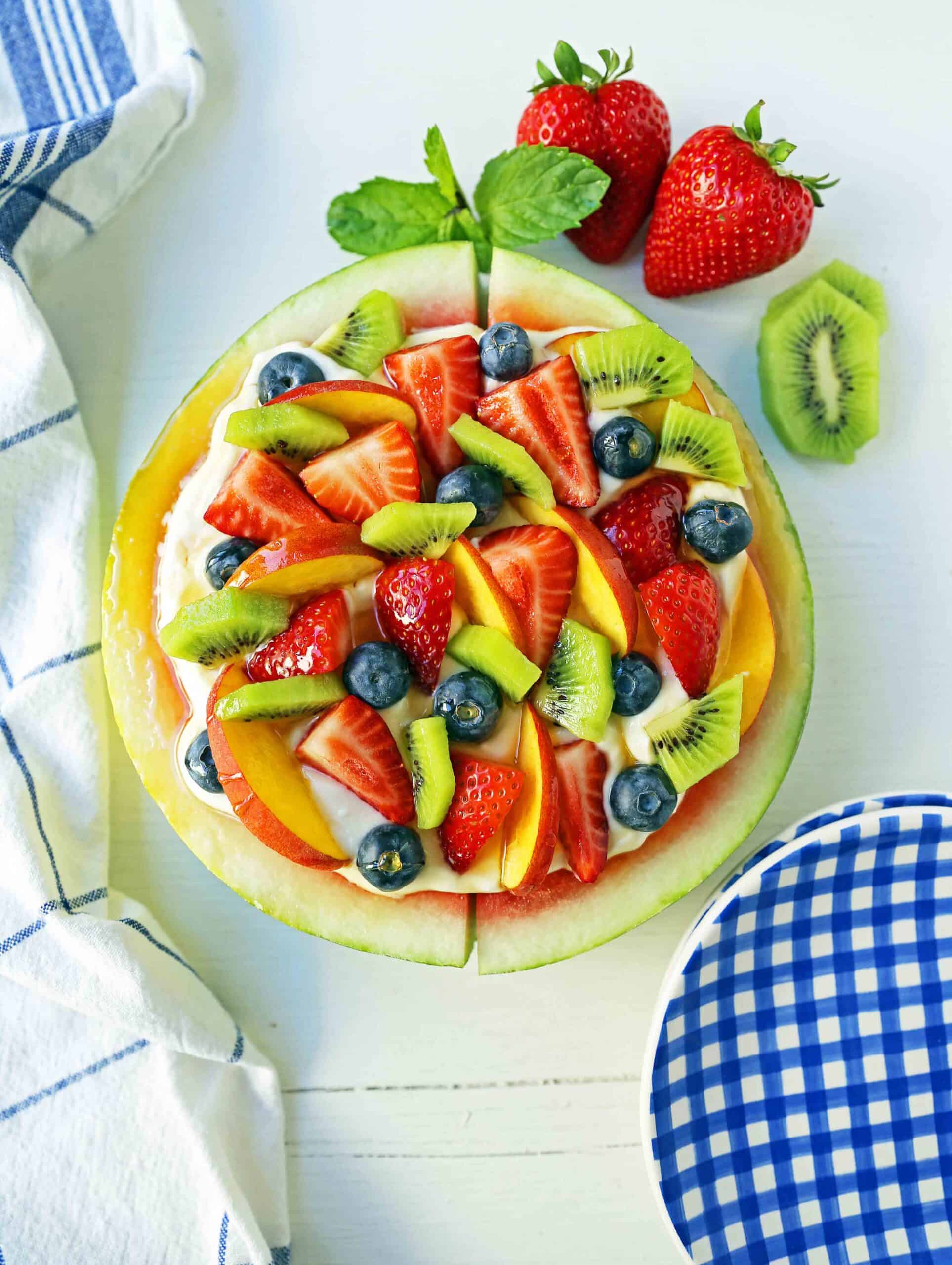 a thick slice of watermelon topped with yogurt and fresh fruit served like pizza.