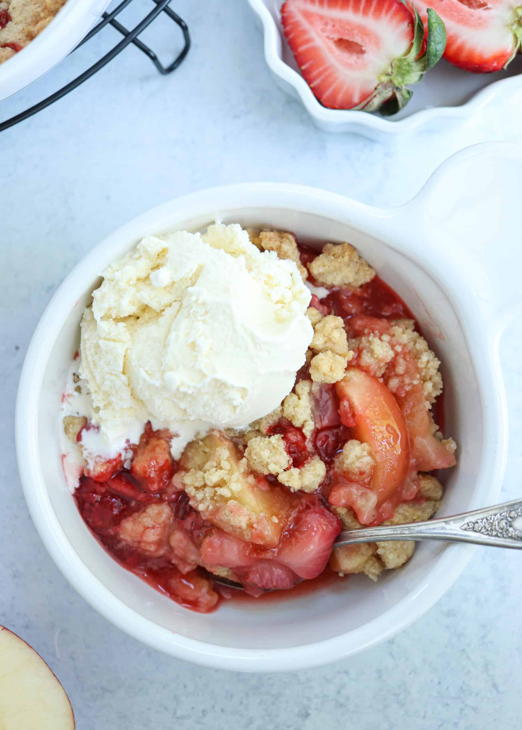 strawberry apple crips in a white bowl topped with vanilla ice cream.