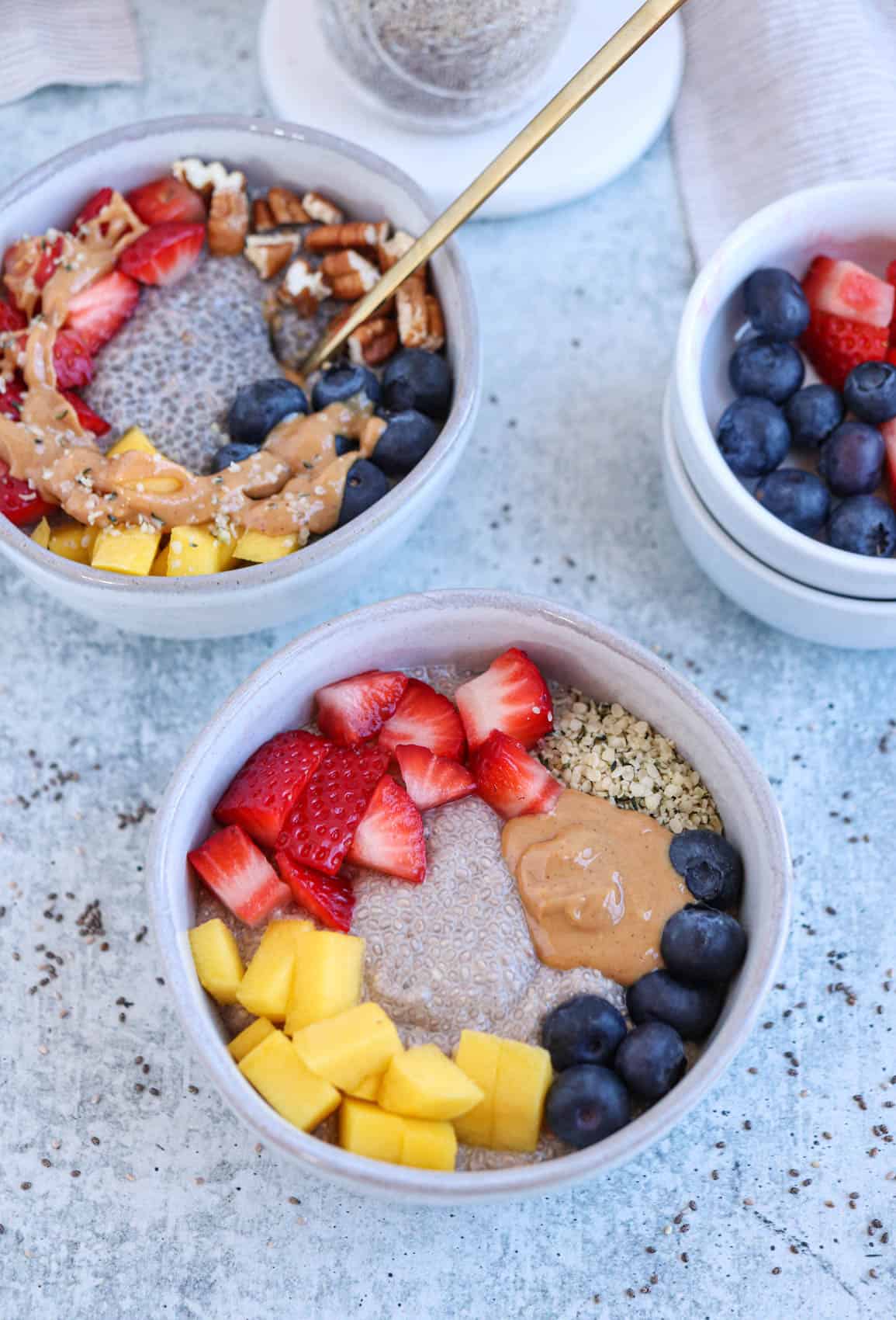 gray bowl with chia pudding, fresh fruit, nut butter and hemp hearts on a light gray surface.