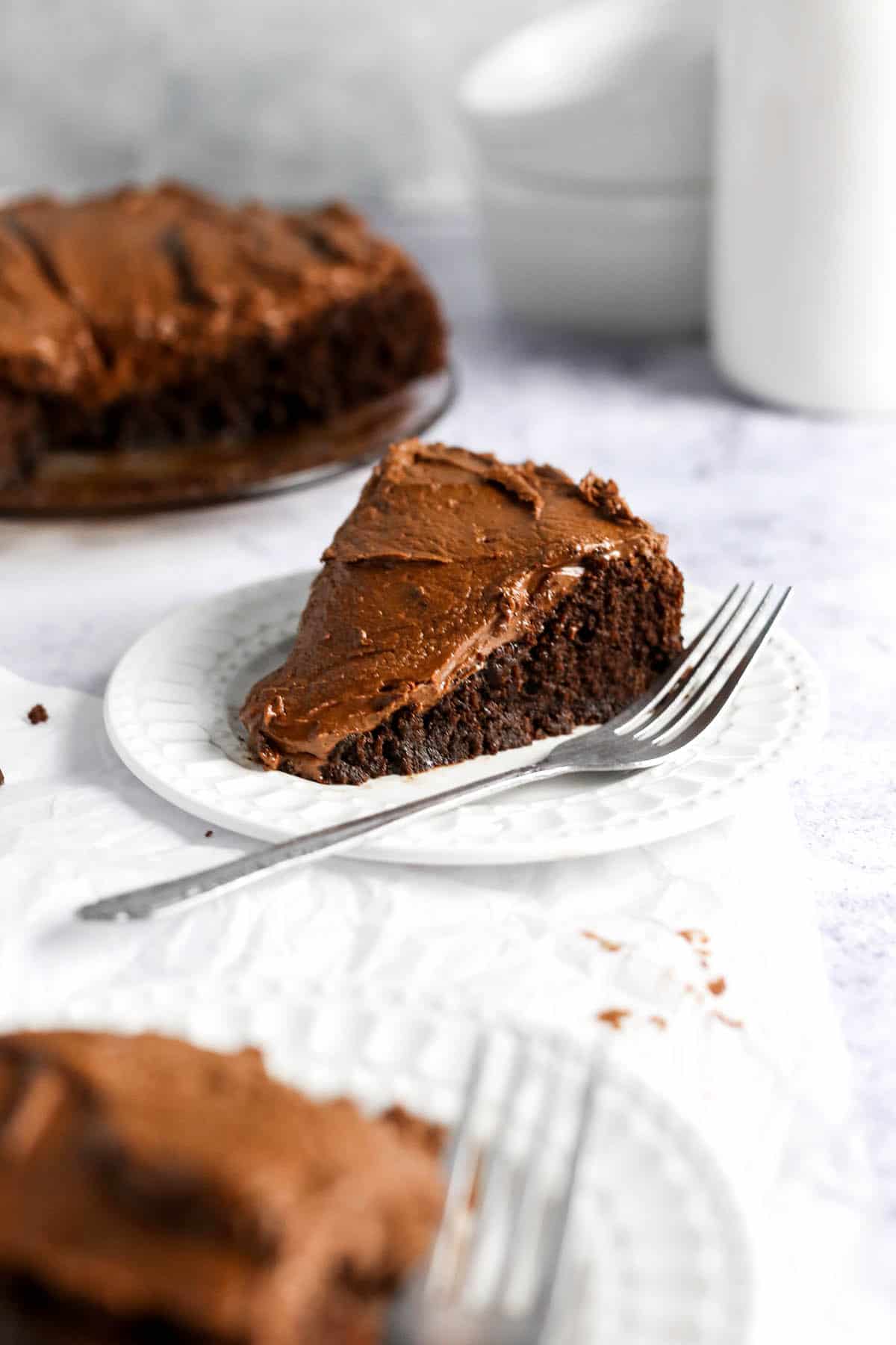 a slice of almond flour chocolate cake with chocolate frosting on a white plate.