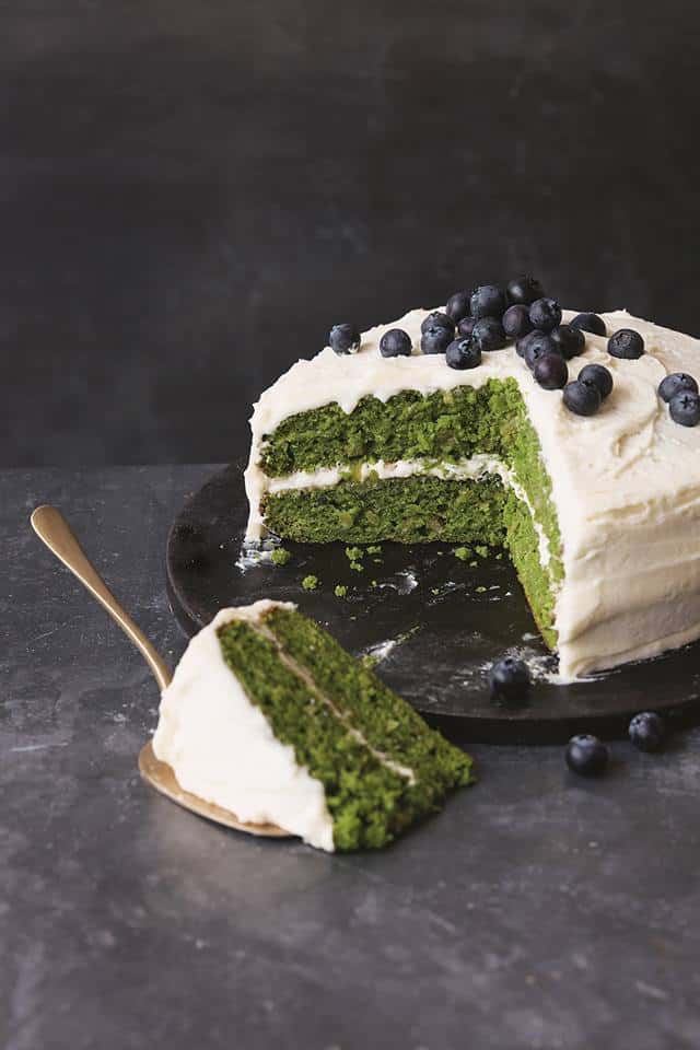 green kale cake with apple icing topped with fresh blueberries on a black plate in dark background.