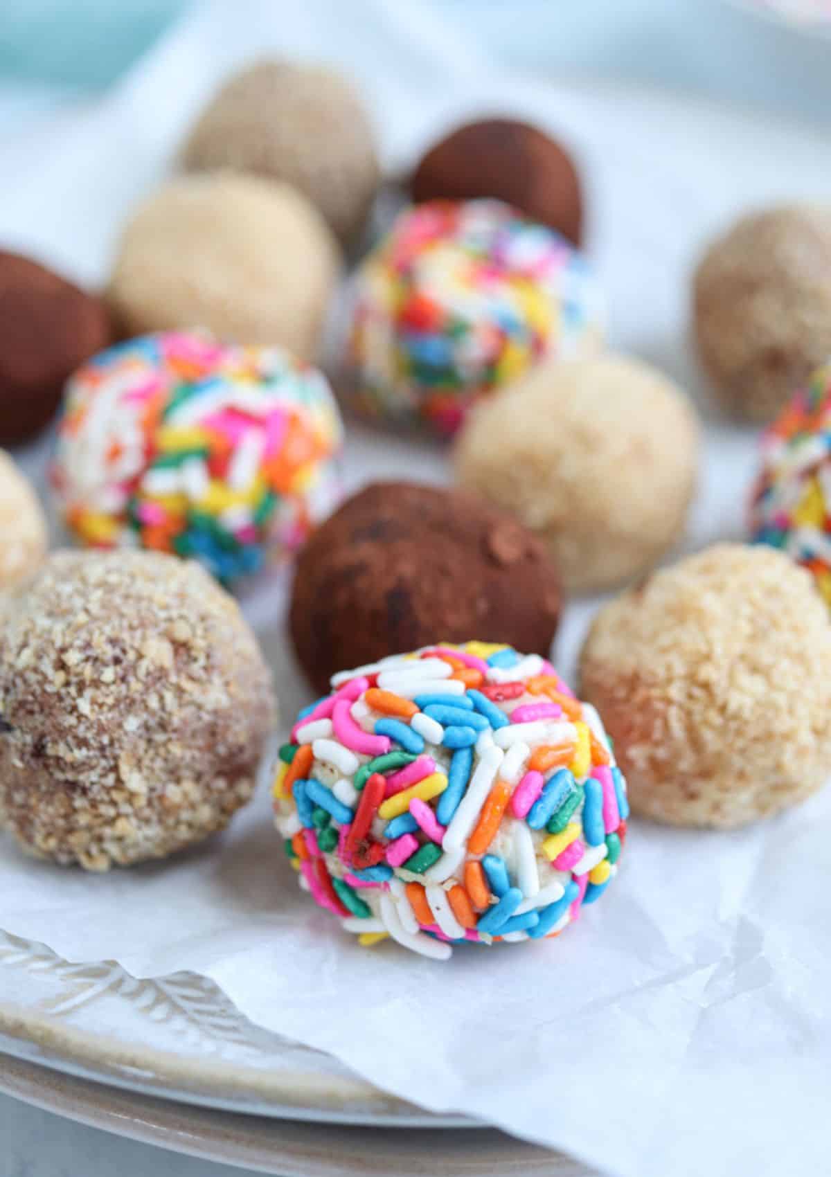 cheesecake balls coated in rainbow sprinkles, cookie crumbs and cocoa powder on a plate.