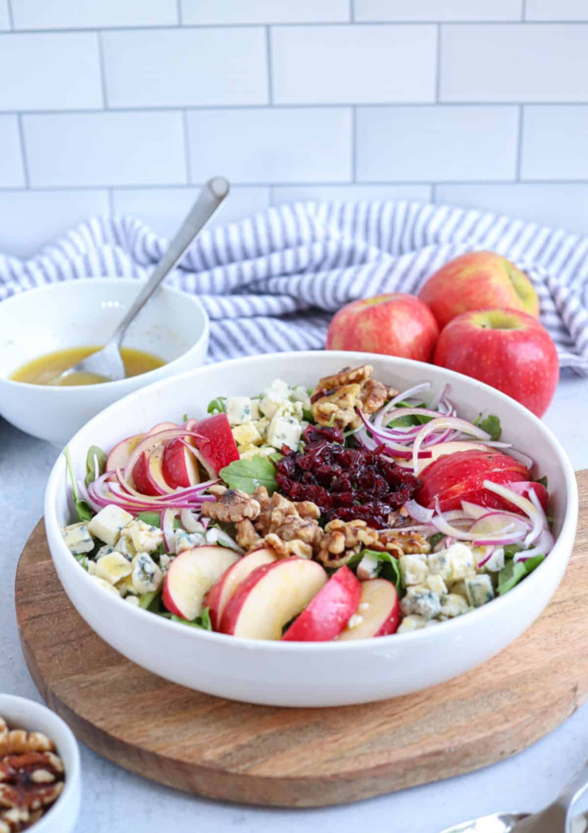 salad with sliced apples and gorgonzola in a white bowl on a wooden board.