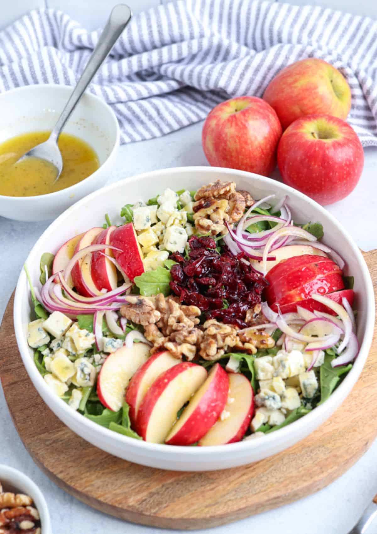 salad with sliced apples and gorgonzola in a white bowl on a wooden board.