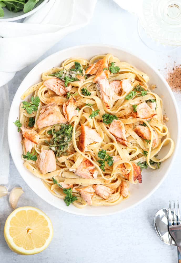 fettucine pasta with salmon and greens in a white bowl. 