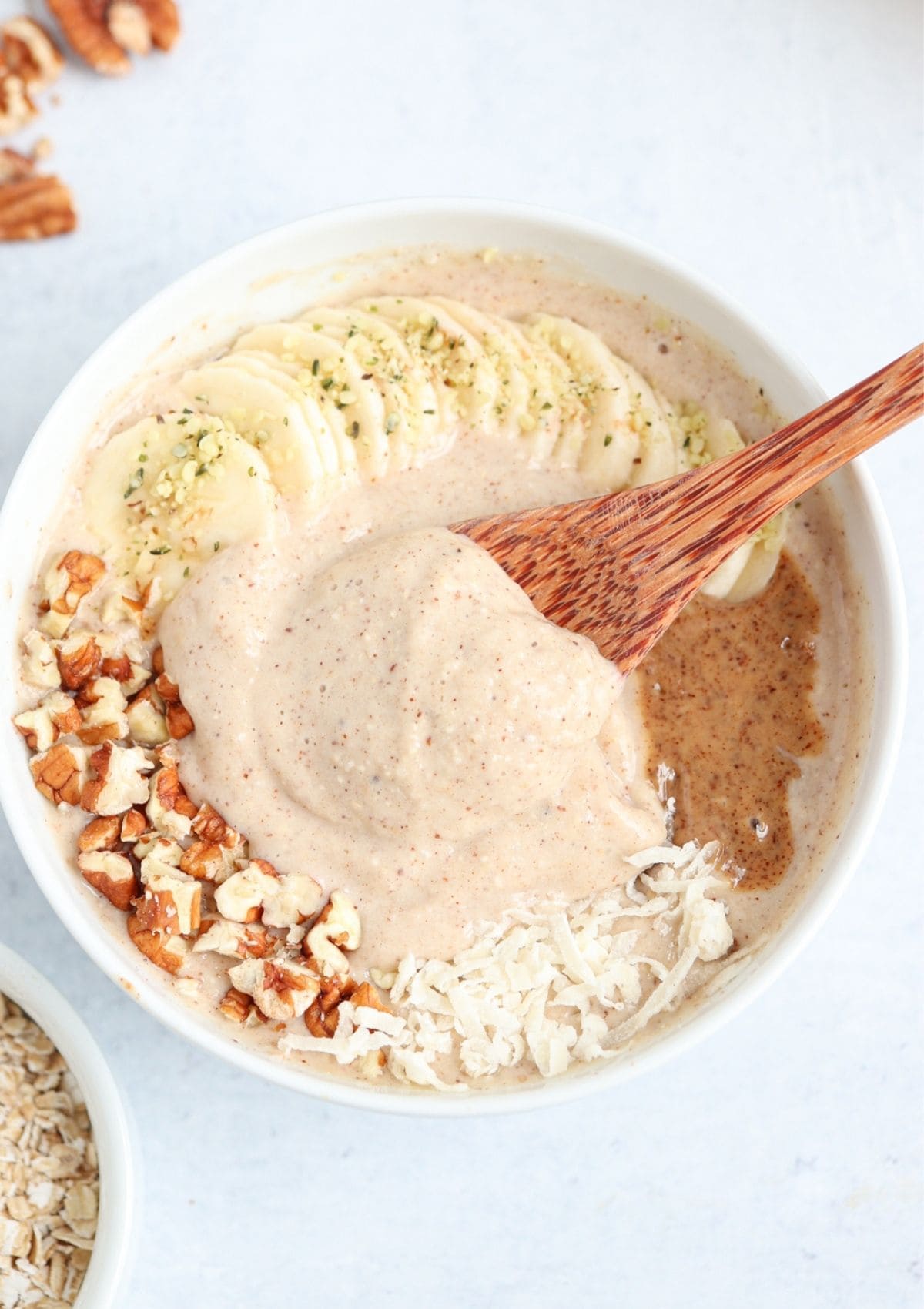 oatmeal smoothie bowl topped with sliced banana, chopped pecans, coconut flakes and almond butter.