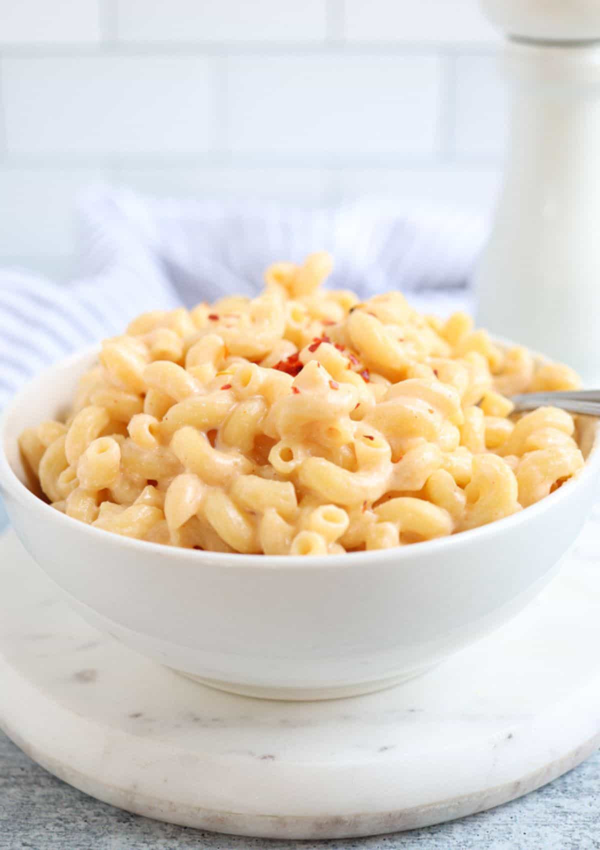 a white bowl of macaroni and cheese on a white marble round board.