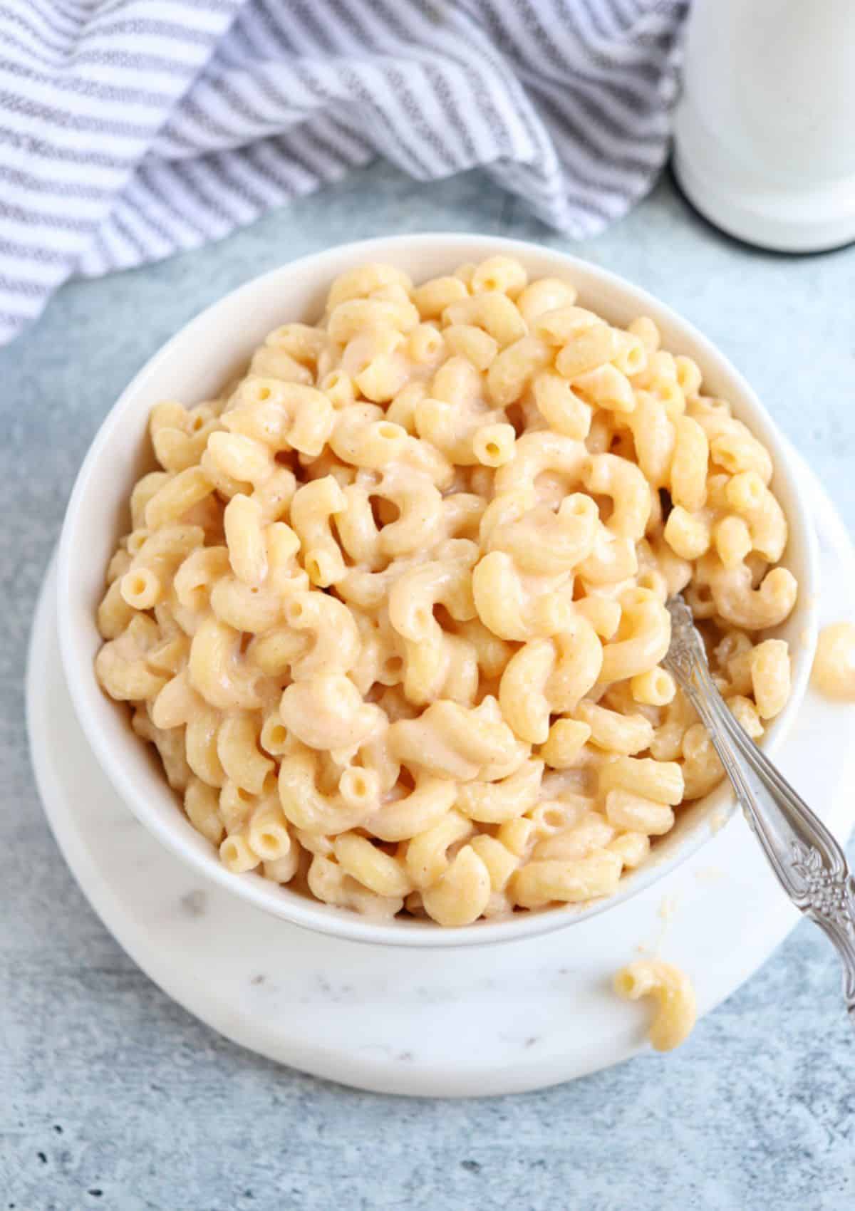 a white bowl of macaroni and cheese on a white marble round board.