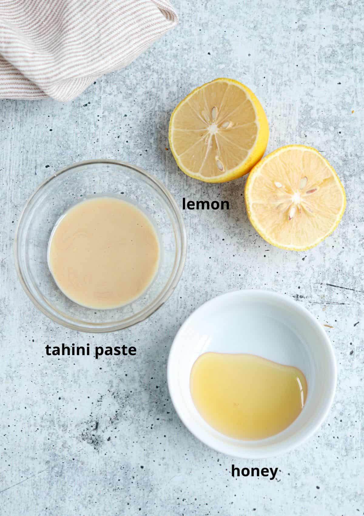 ingredients for making lemon tahini sauce on gray background with captions. 