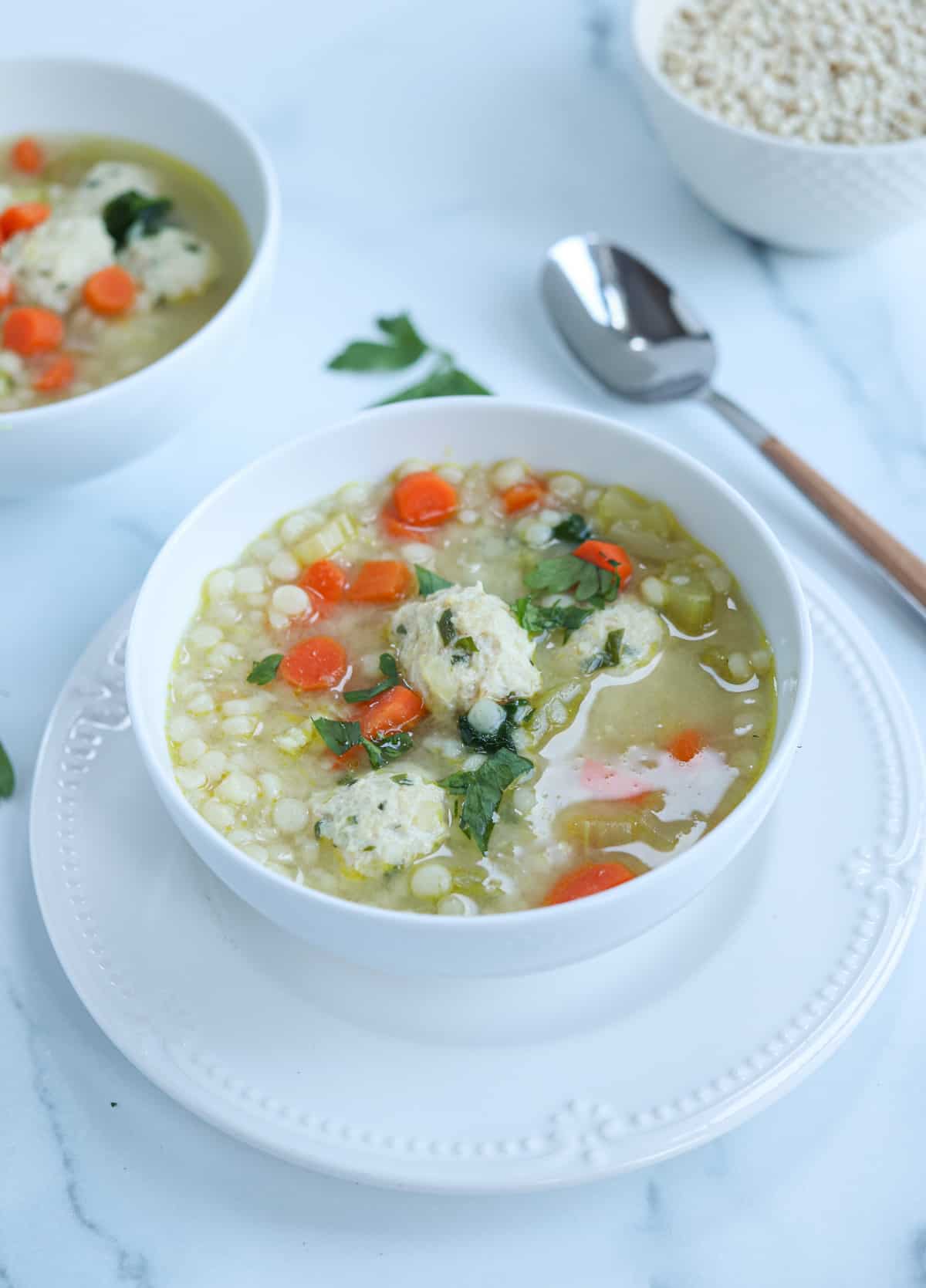 a bowl of chicken meatball soup with pearl couscous, carrots and parsley.