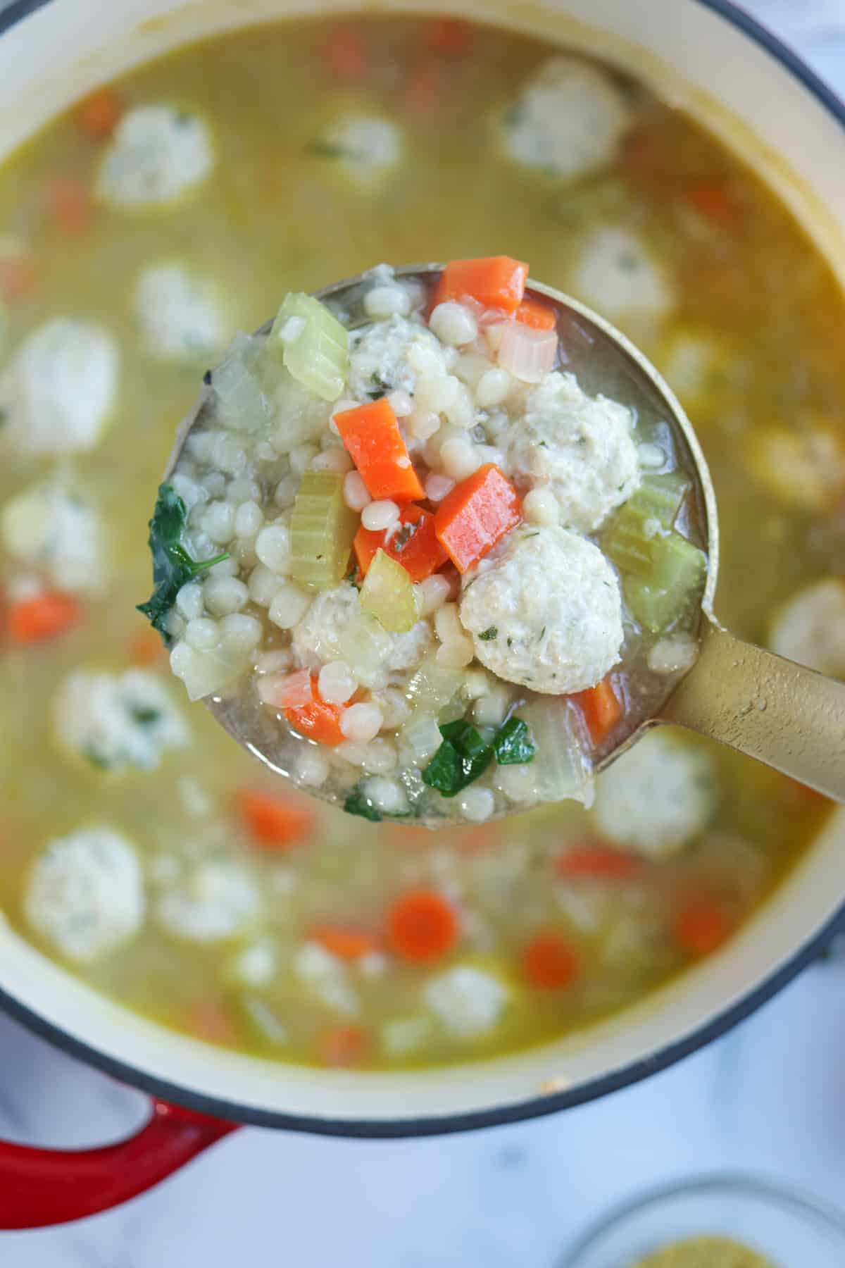 chicken meatball soup with pearl couscous, carrots, celery and parsley on a ladel.
