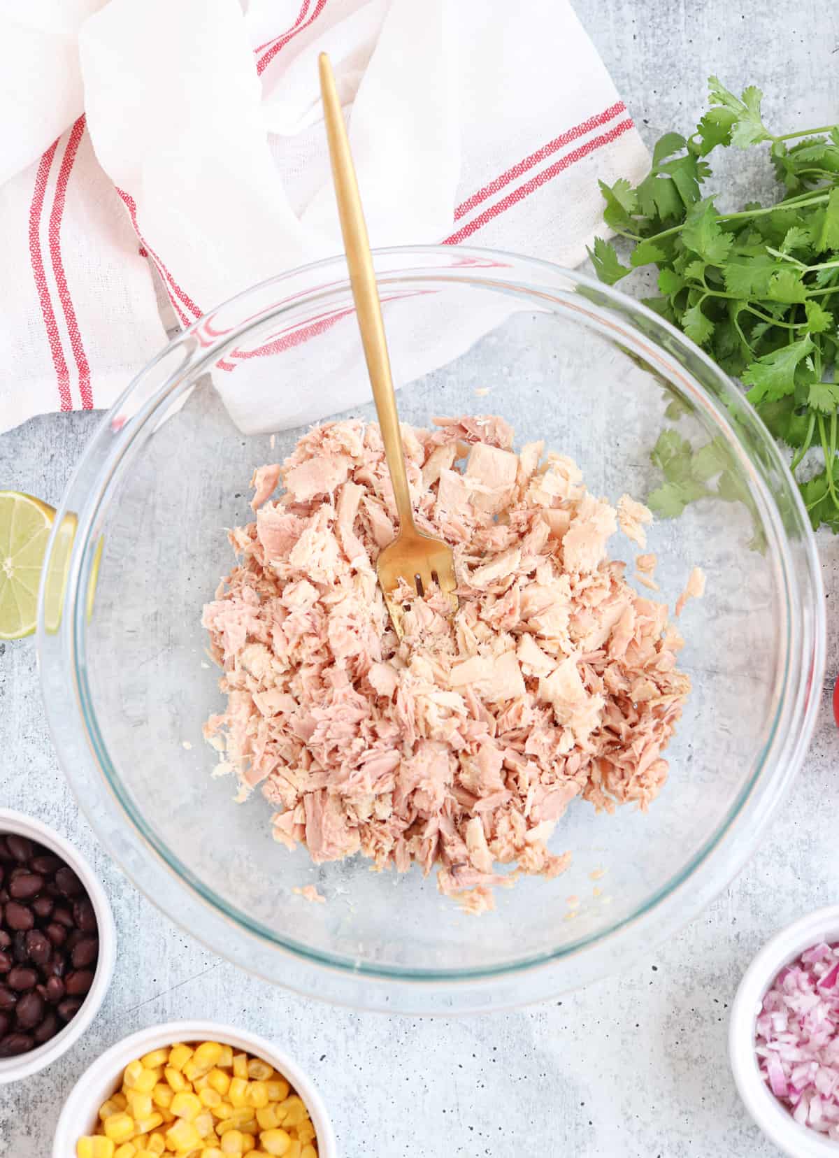 canned tuna in a glass bowl being broken down with a fork.