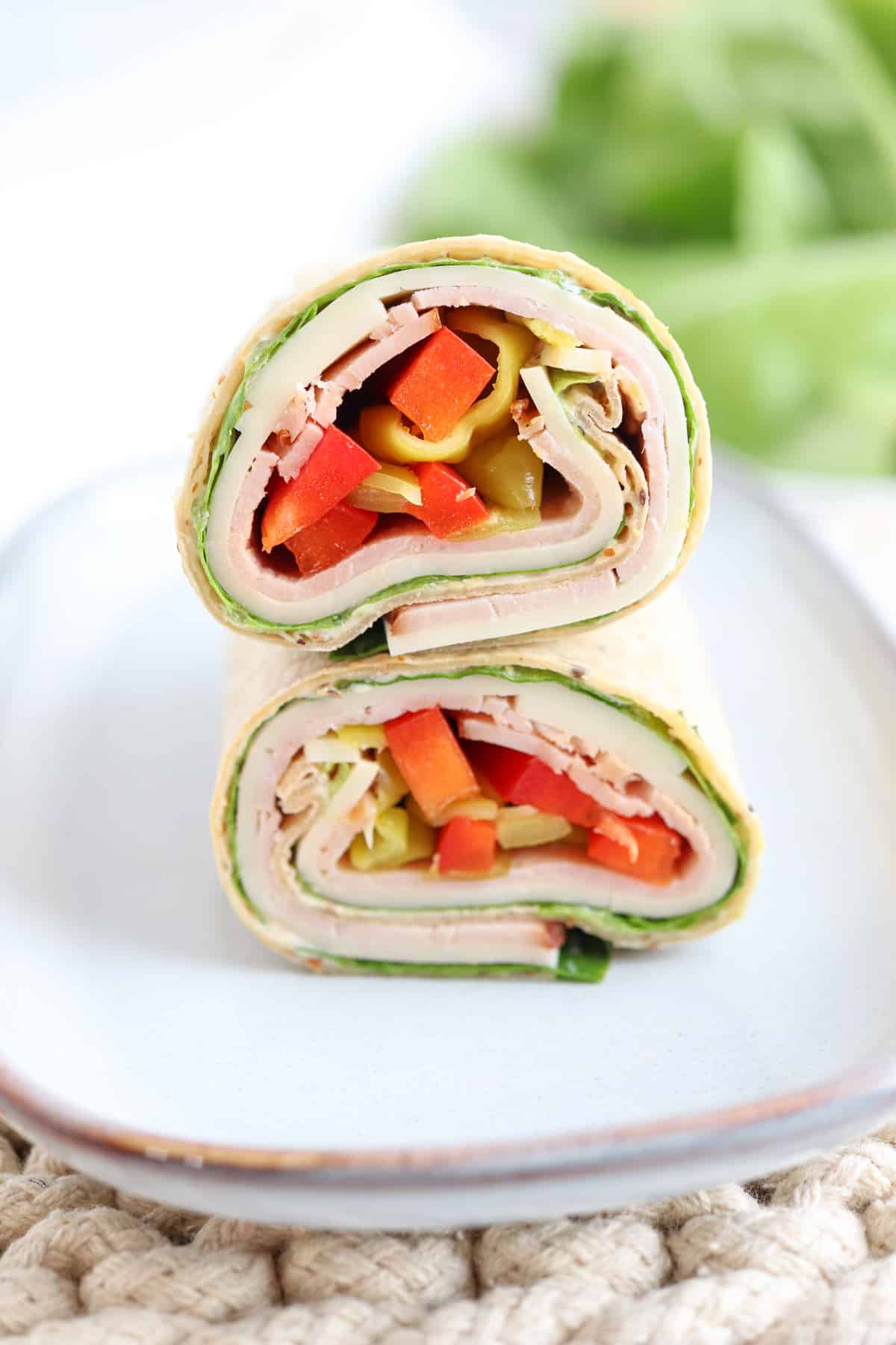 ham and cheese wrap with red peppers and pepperoncini on a plate.