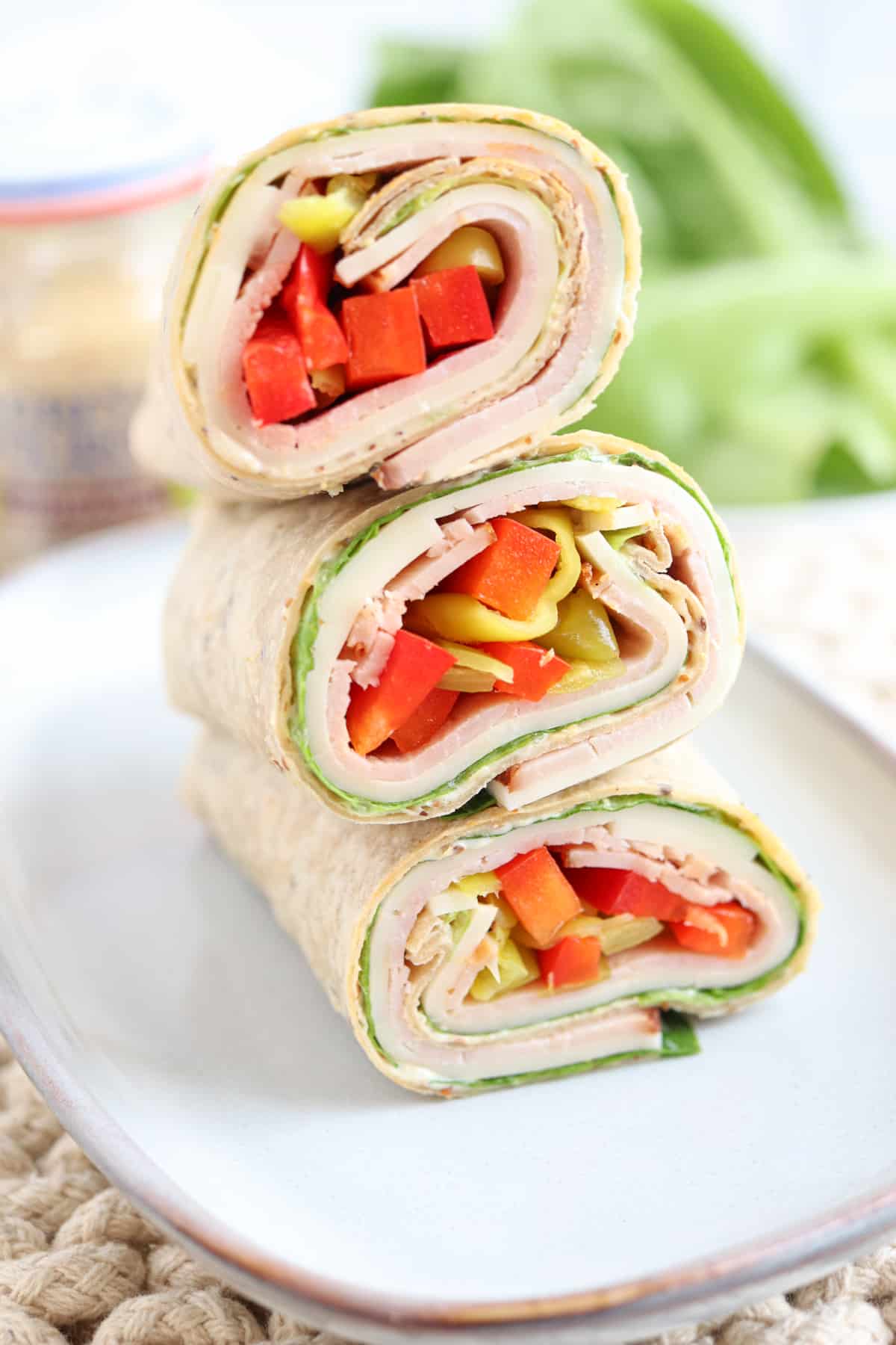 ham and cheese wrap with red peppers and pepperoncini on a plate.