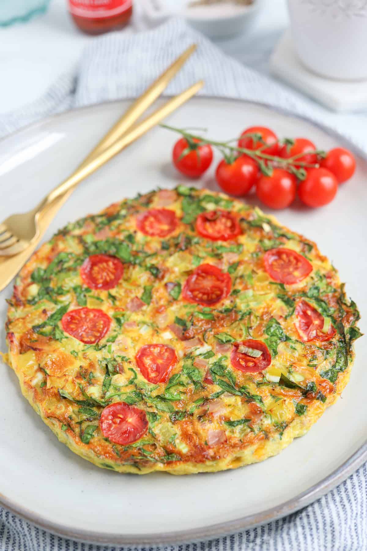 an omelette made in the air fryer with cheese, ham, spinach and cherry tomatoes on a light gray plate.