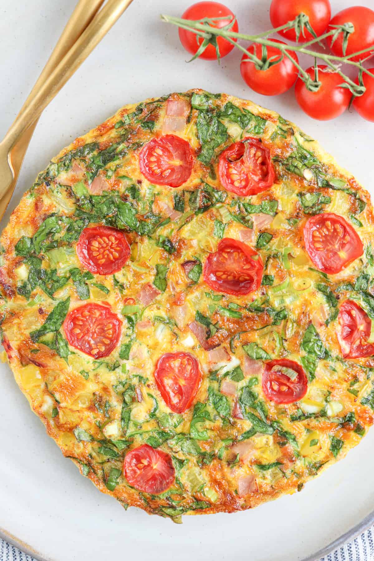 an omelette made in the air fryer with cheese, ham, spinach and cherry tomatoes on a light gray plate.