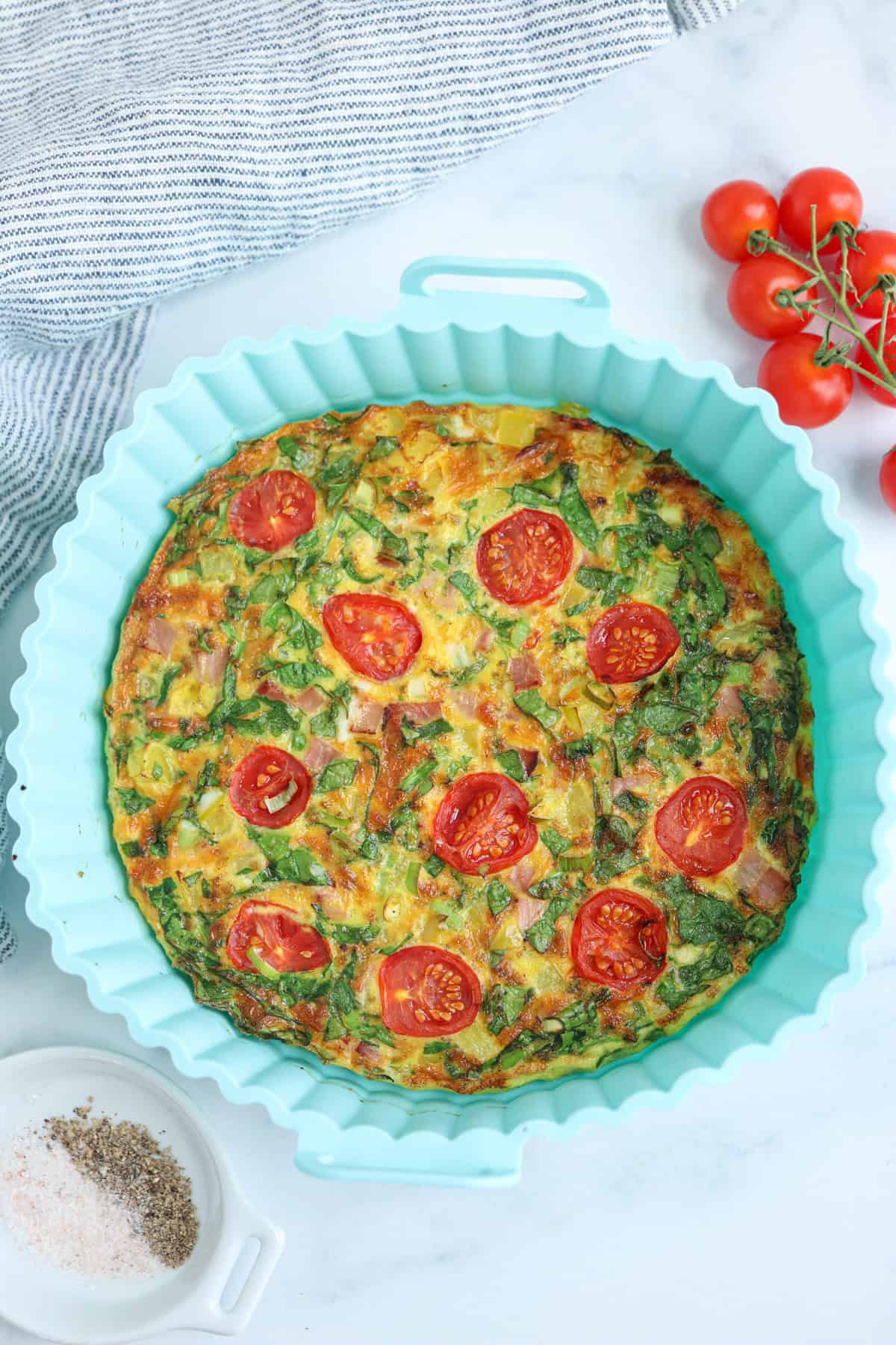 an omelette made in the air fryer with cheese, ham, spinach and cherry tomatoes in a light blue silicome tray.
