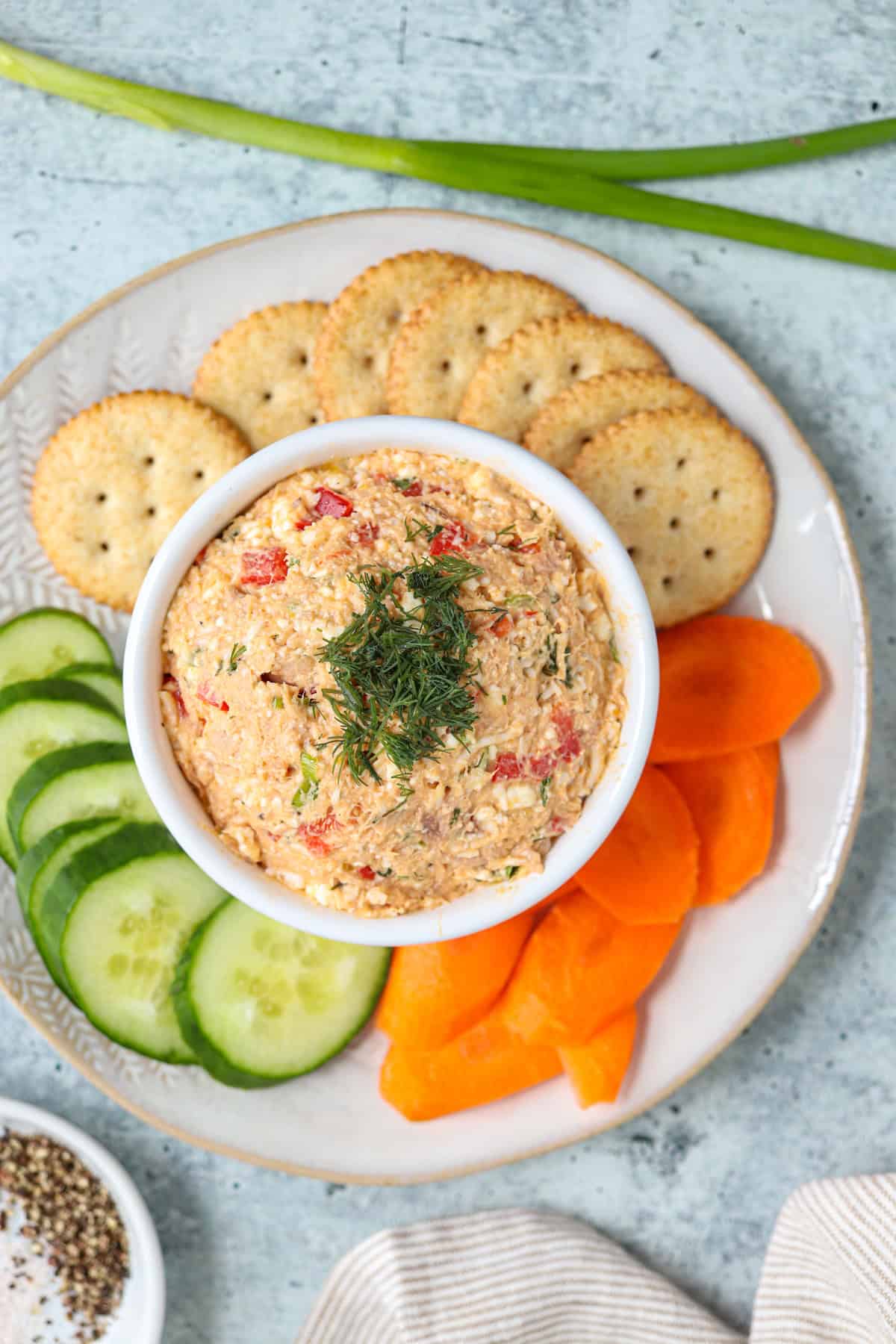 tuna spread in a white bowl on a plate surrounded by vegetables and crackers. 