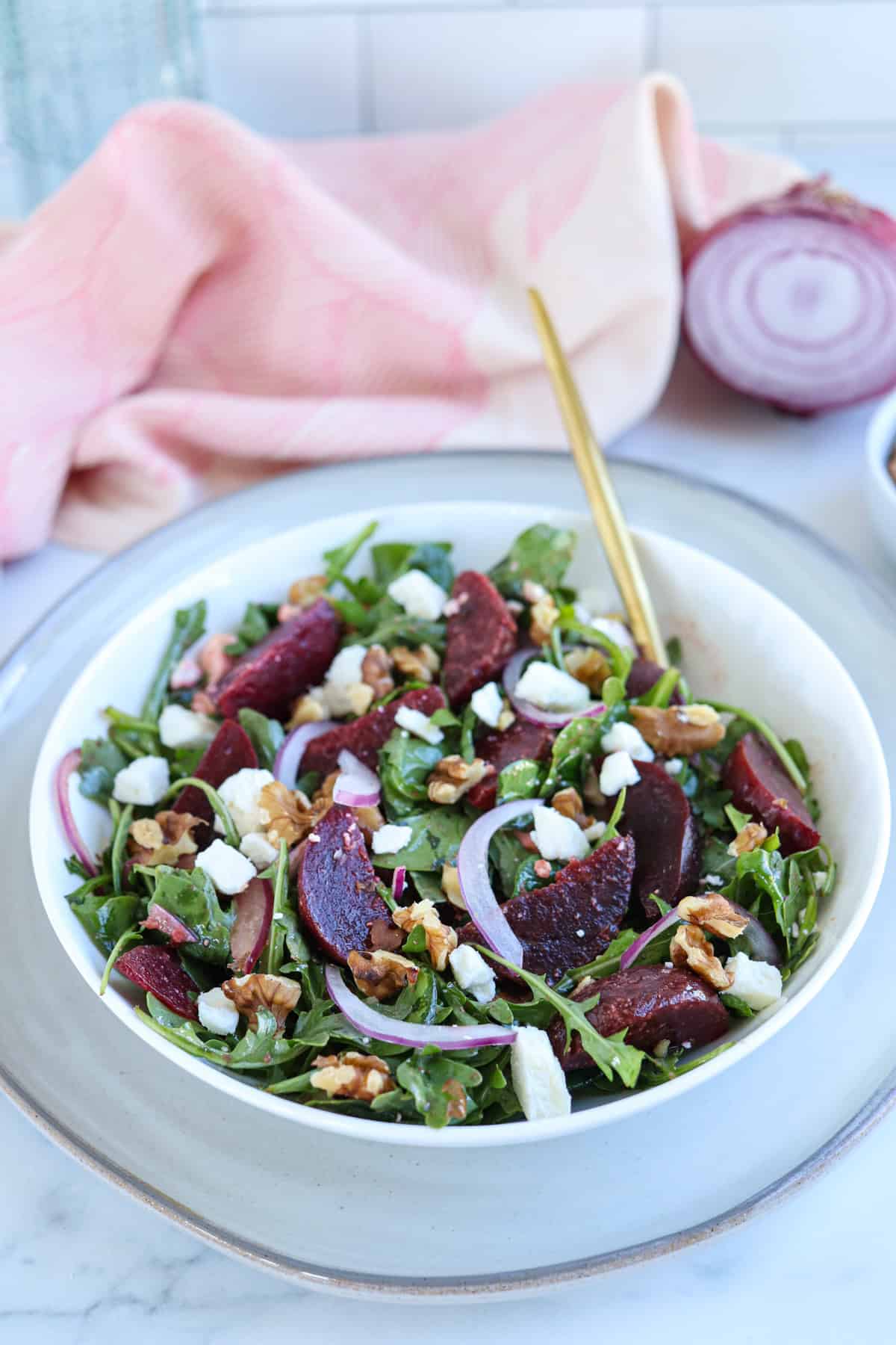 beet and feta cheese salad on a bed of greens, sliced onions and walnuts in a white bowl.