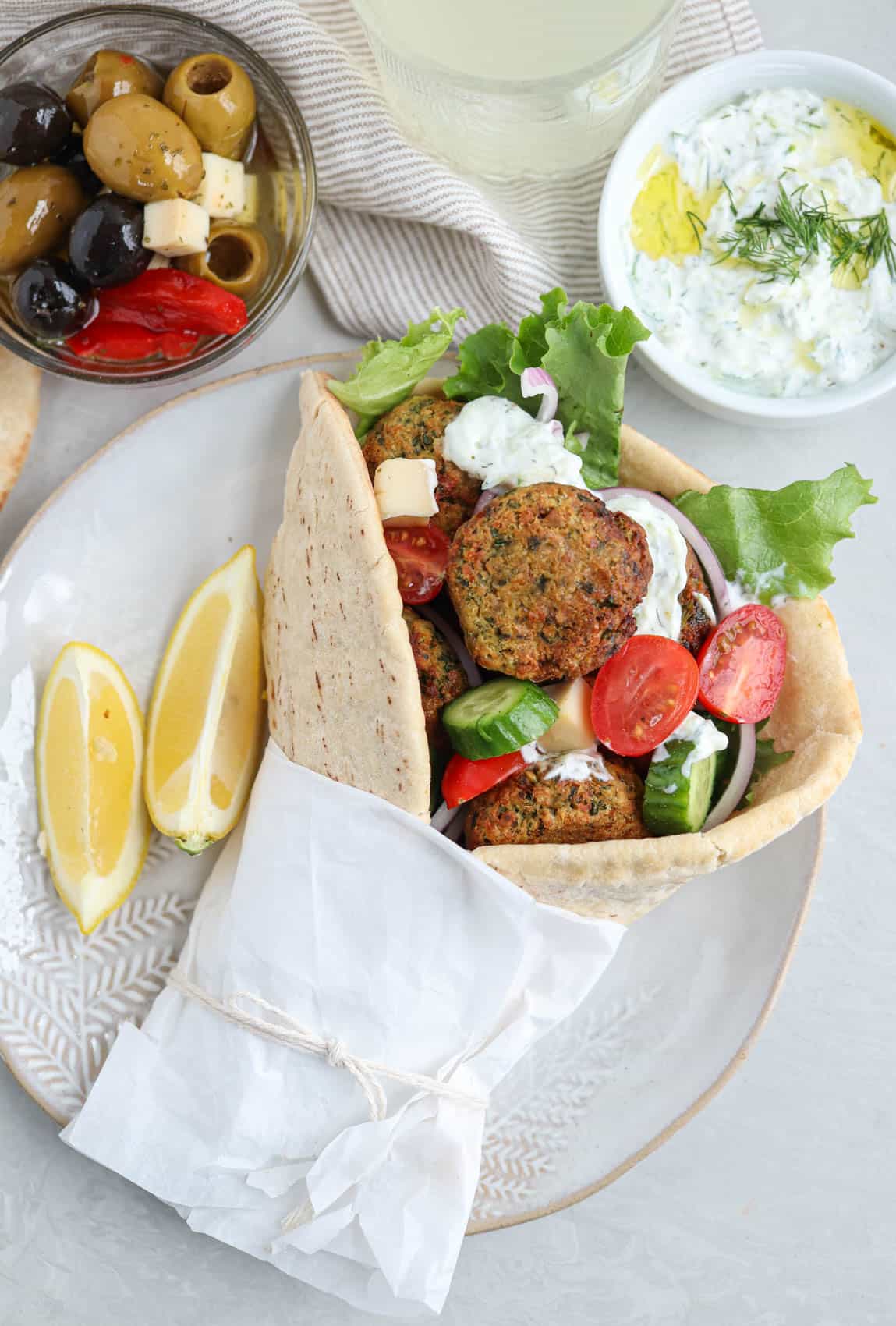 falafel pita sandwich with fresh vegetables on a plate with a side of tzatziki and olives.