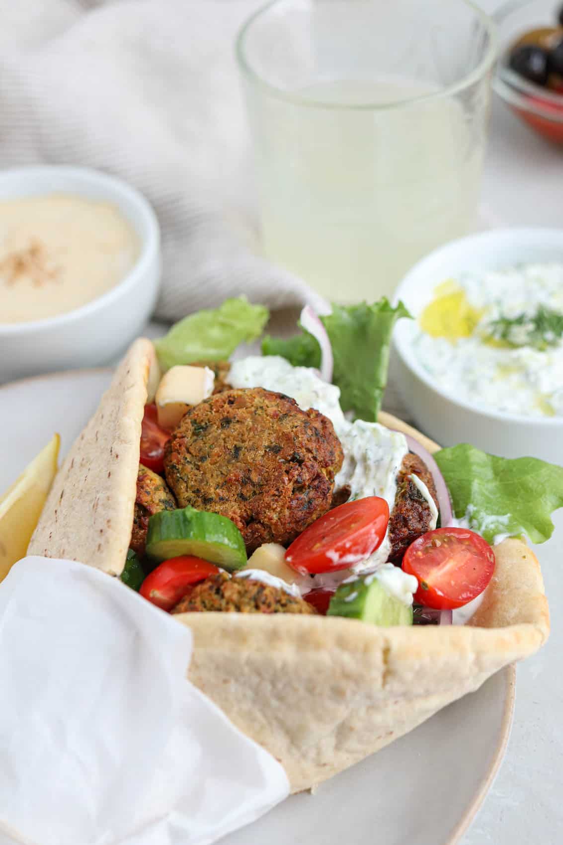 falafel pita sandwich with fresh vegetables wrapped in paper on a plate.