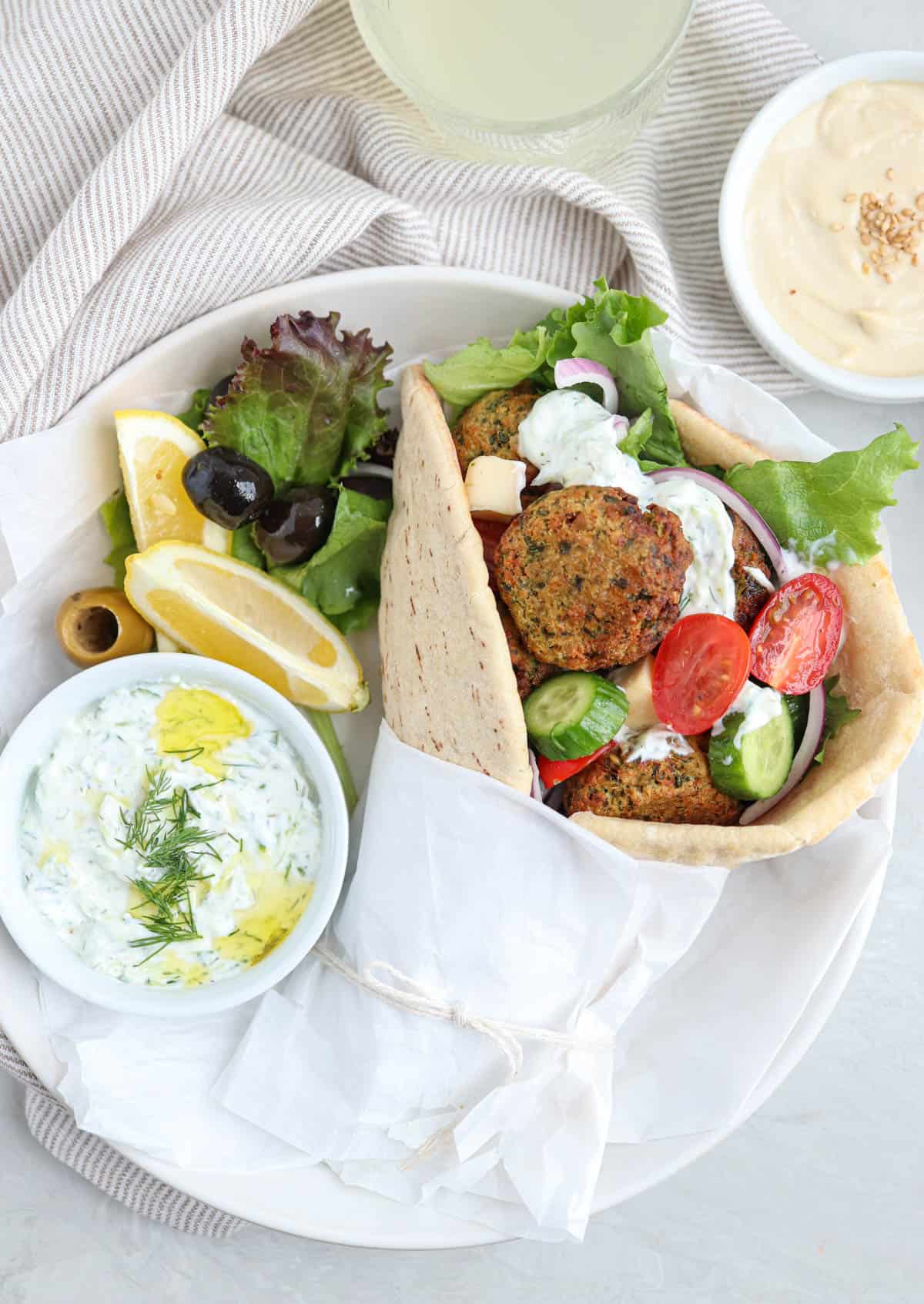 falafel pita sandwich with fresh vegetables on a plate with a side of tzatziki and olives.