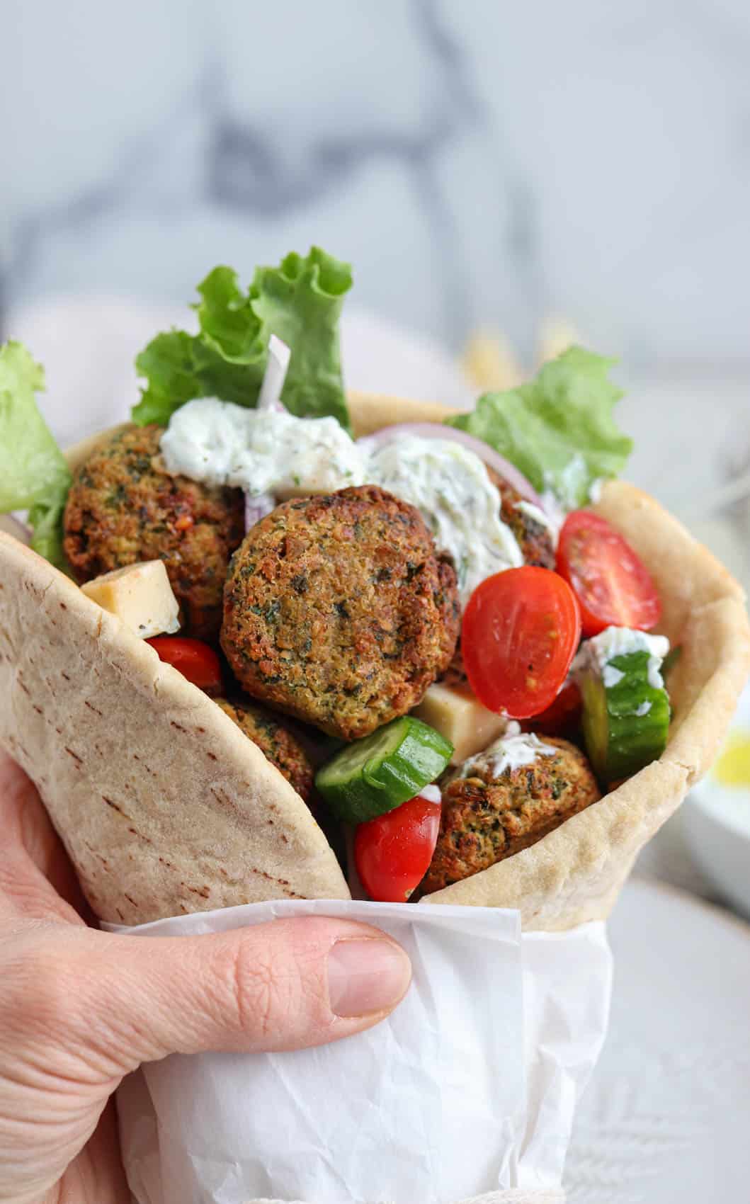 falafel pita sandwich with fresh vegetables and tzatziki held with a hand.