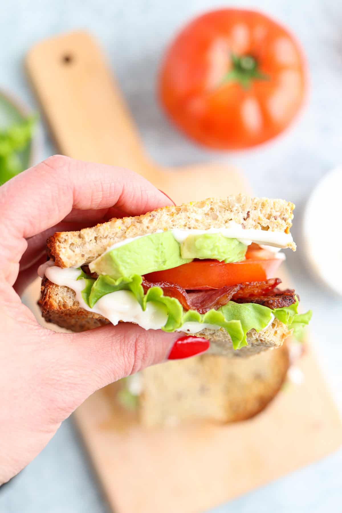 bacon lettuce avocado tomaton sandwich on toasted bread held by a hand.