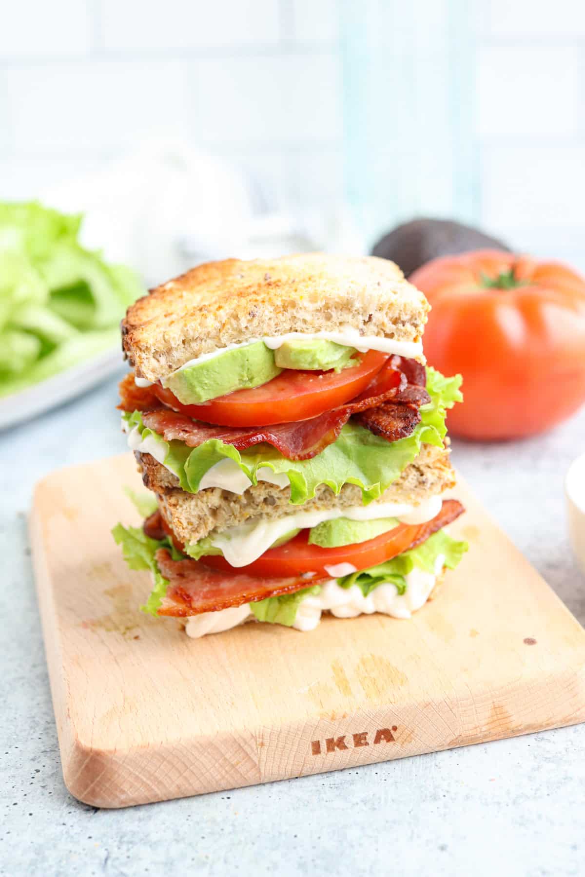 bacon lettuce tomato avocado sandwich stacked on a wooden board.