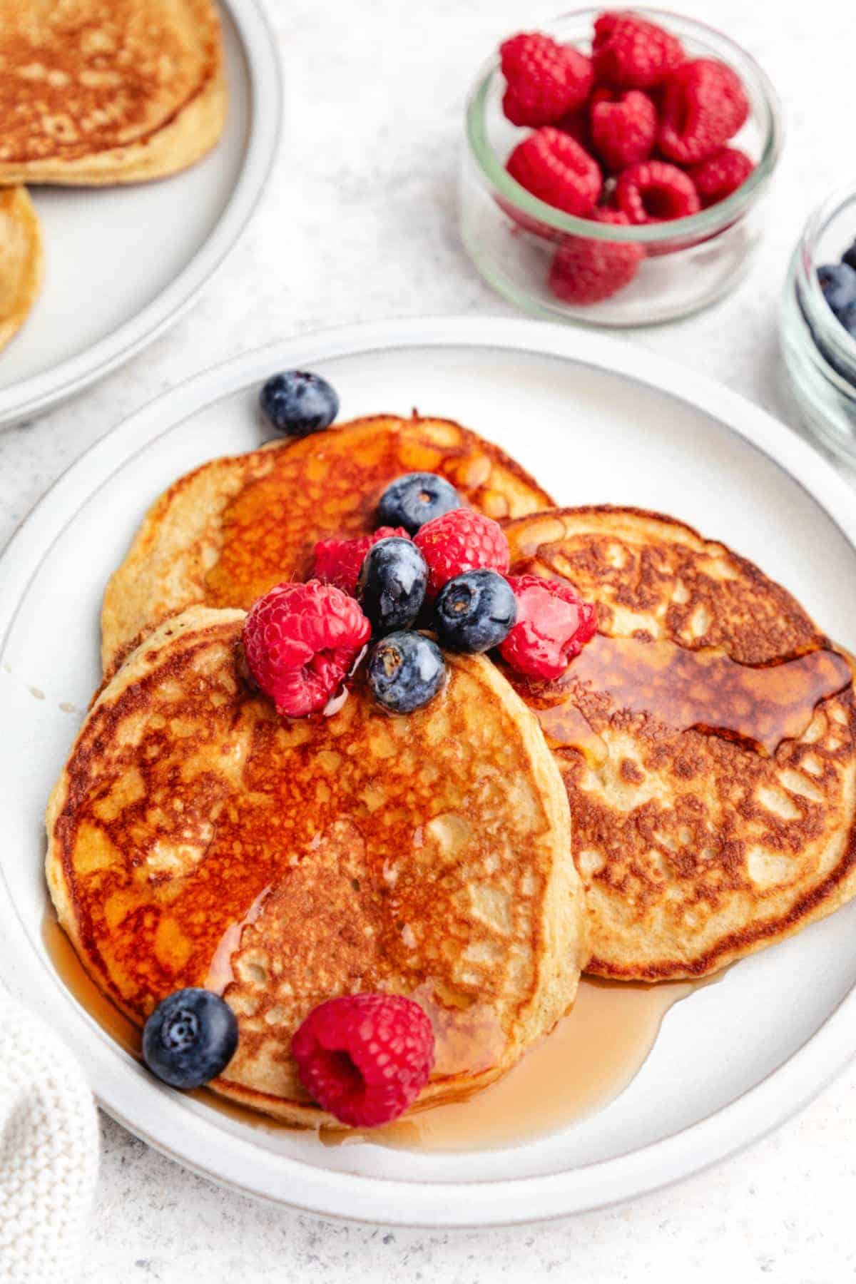 cottage cheese pancakes on a white plate with berries and maple syrup.